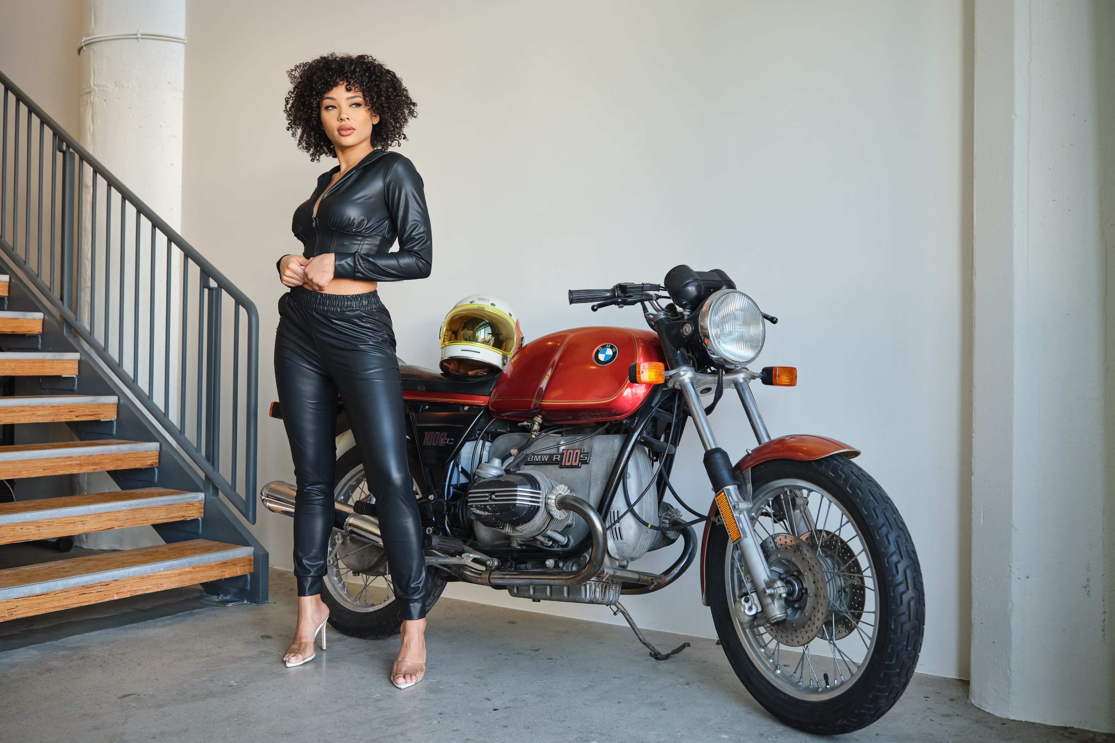 A woman in a black outfit stands next to a vintage BMW motorcycle in a modern indoor setting.