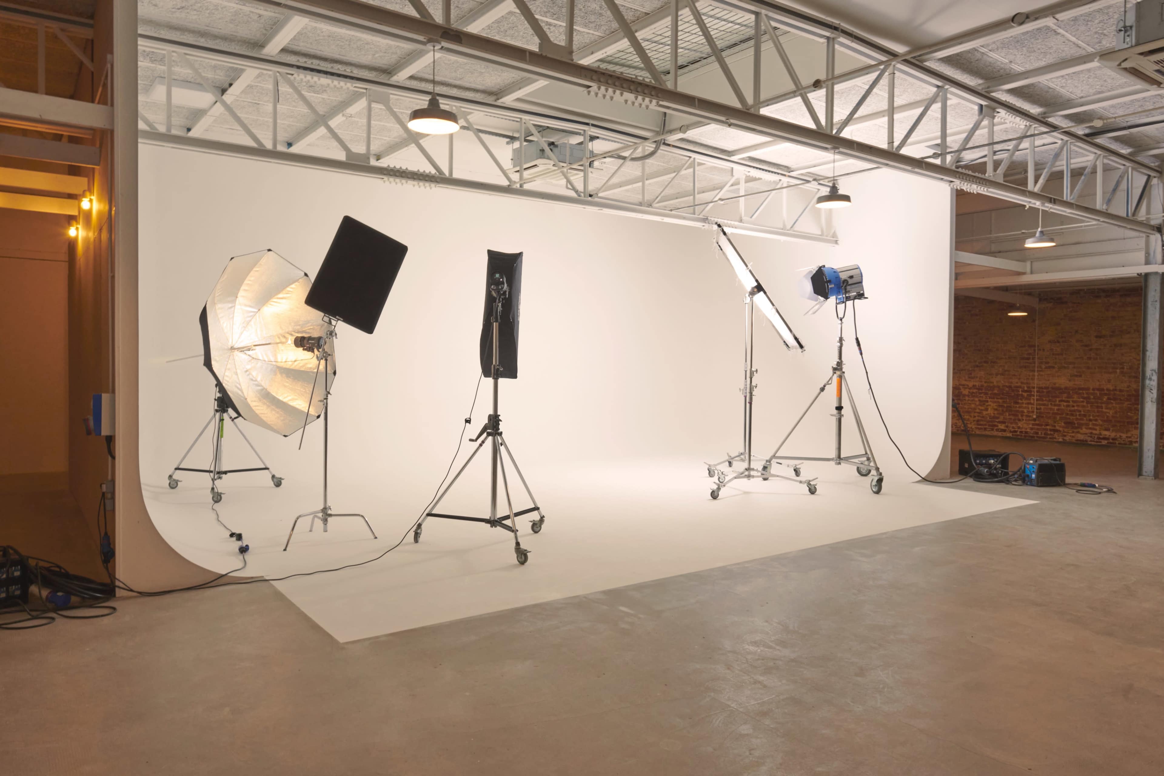 The image shows a photography studio with various lighting equipment set up against a plain white backdrop.
