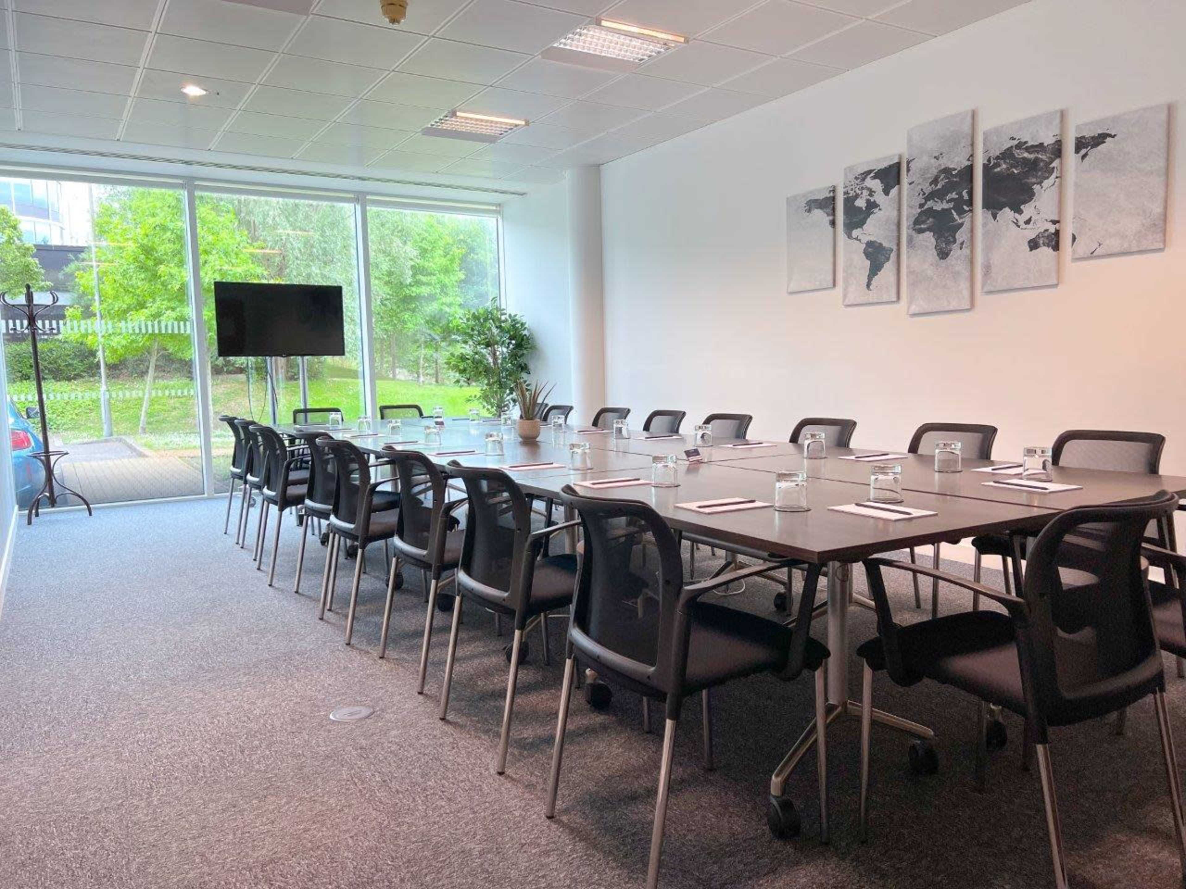 The image shows a modern conference room with a long table, black chairs, and a large window overlooking greenery.