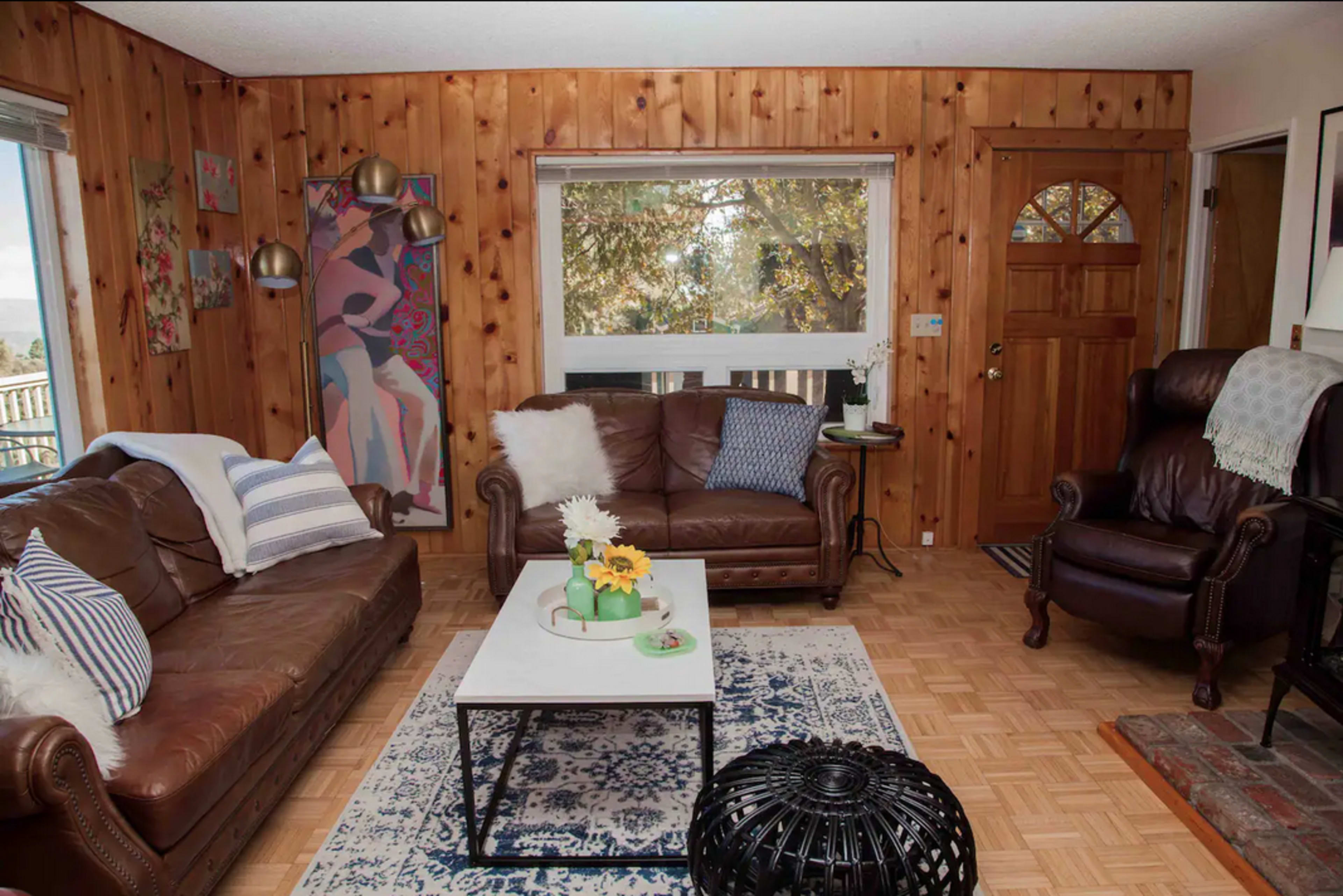 A cozy living room with two leather sofas, a coffee table on a patterned rug, and a wooden door that leads outside.