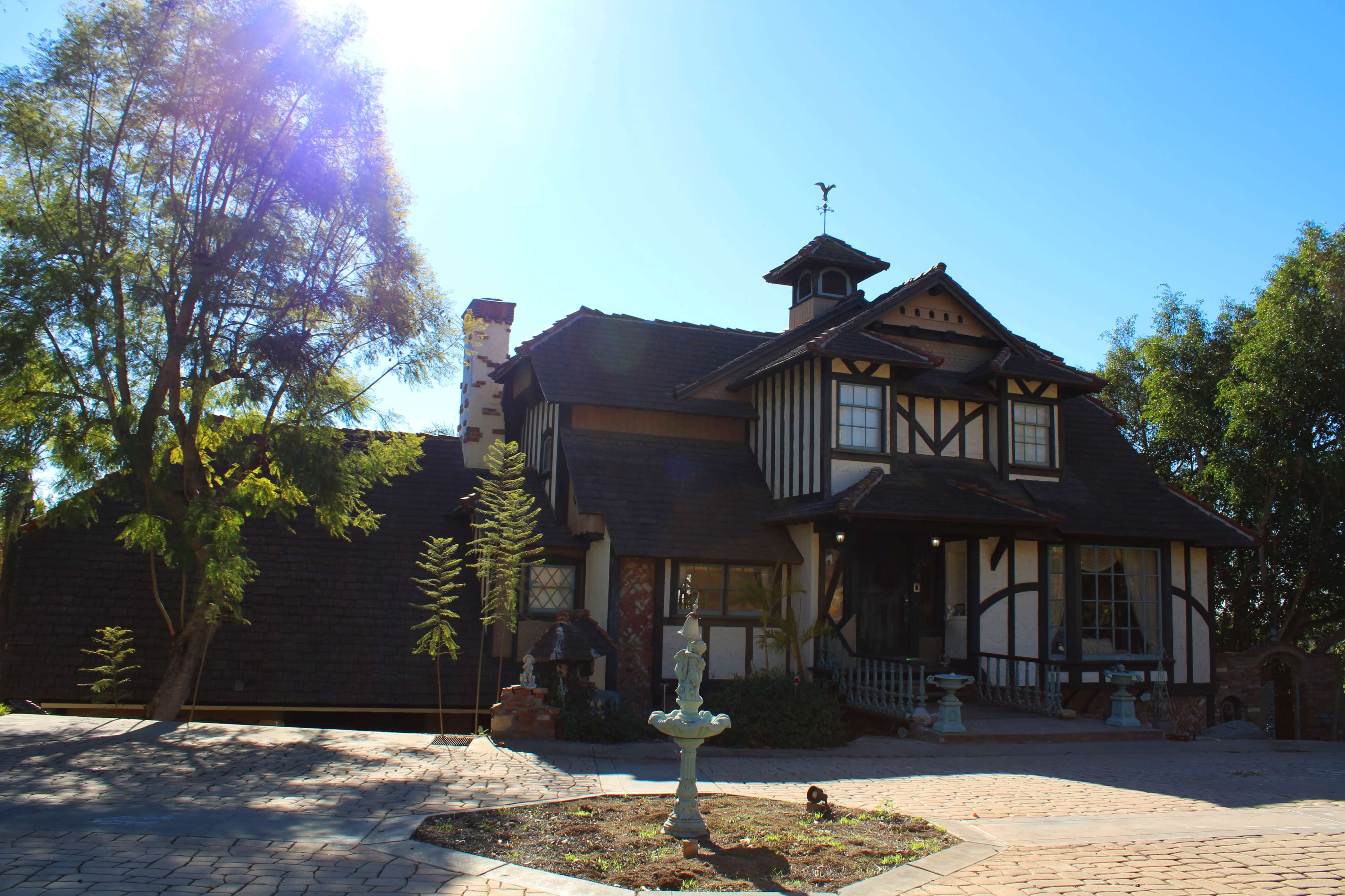 A large, two-story house with a steeply pitched roof and decorative timber framing is set against a clear blue sky.