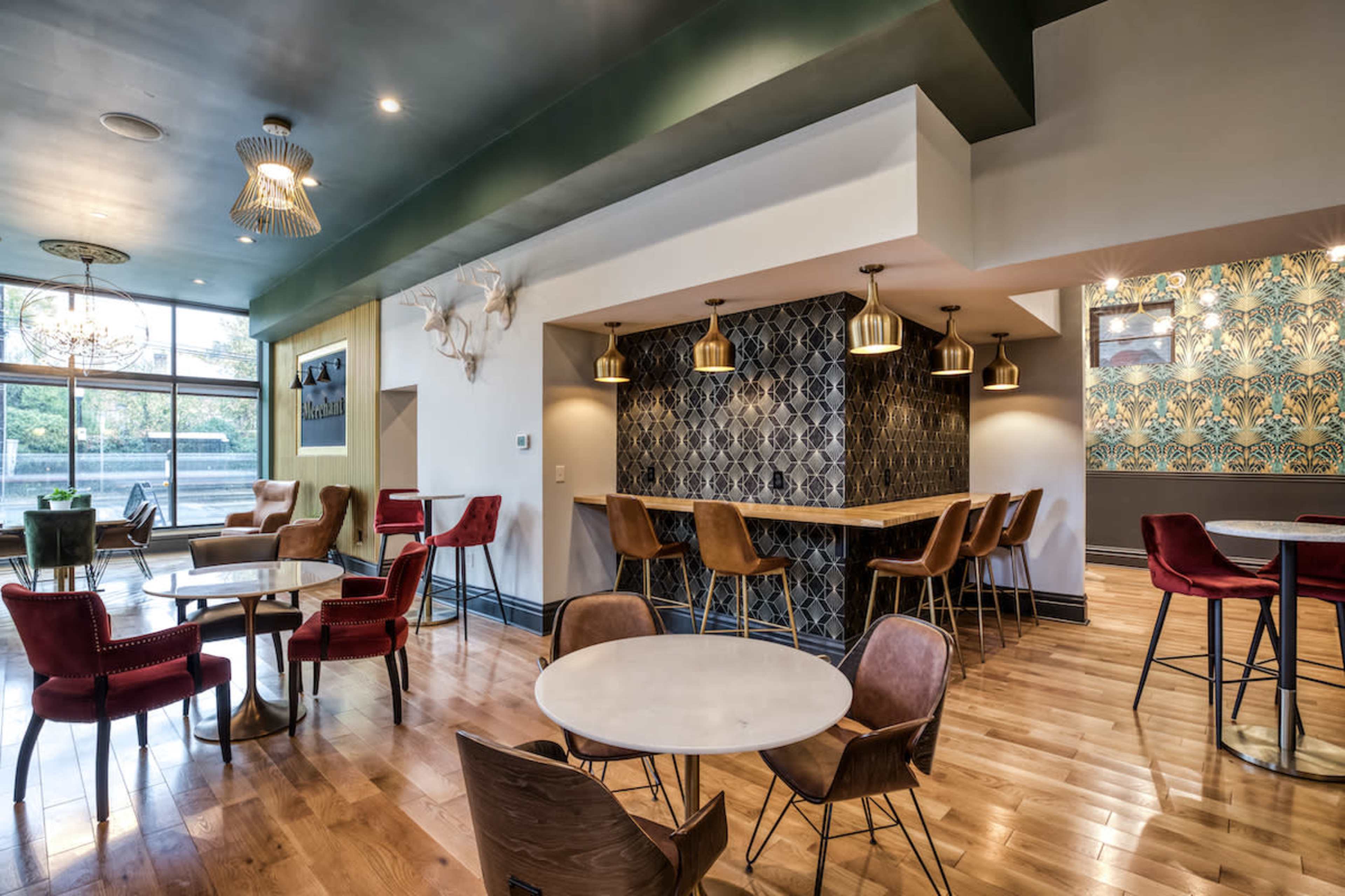 A modern café interior featuring wooden floors, a mix of tables and seating, and decorative light fixtures.