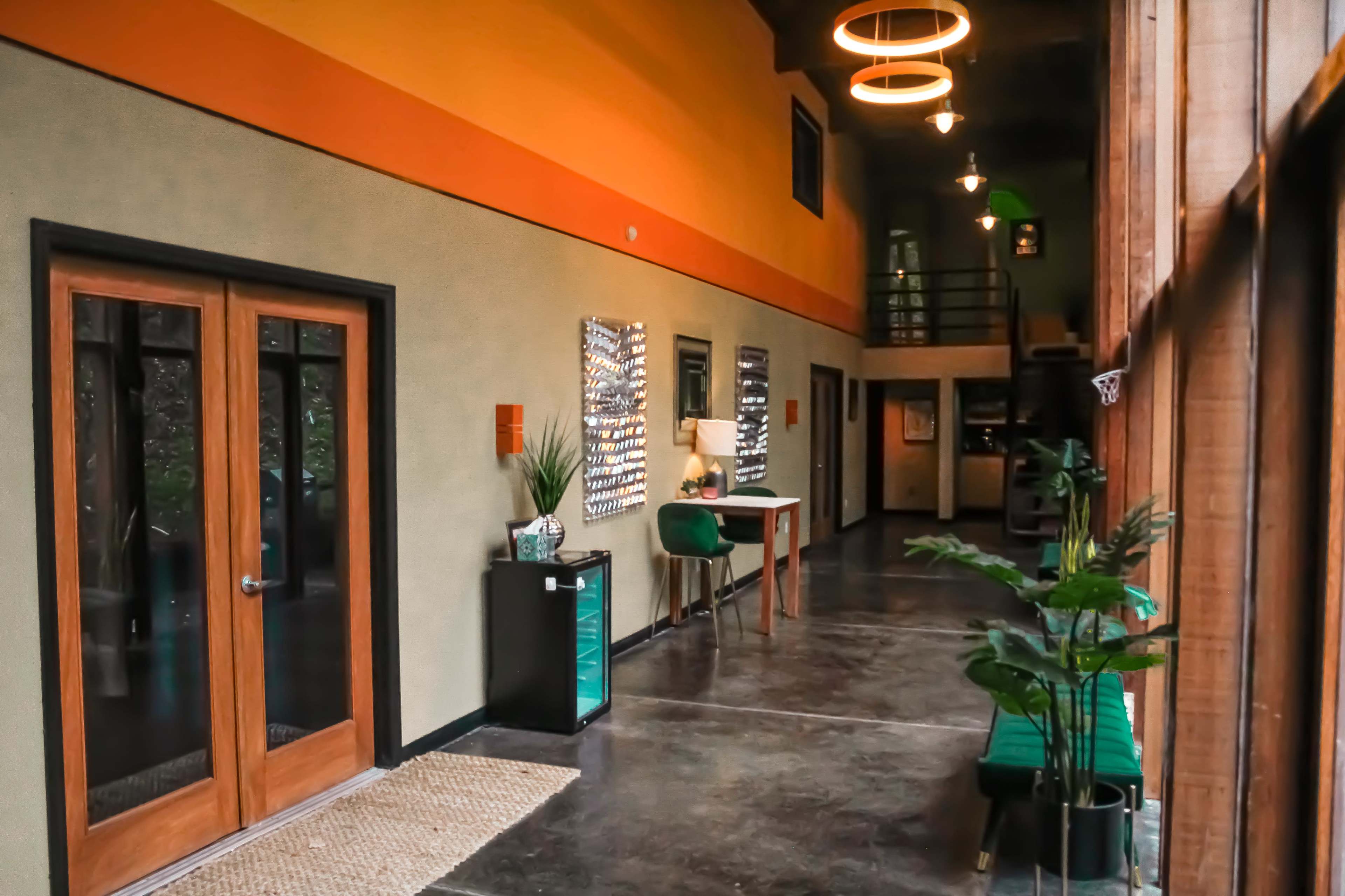 A hallway with wooden doors, green plants, and a table is illuminated by circular pendant lights.