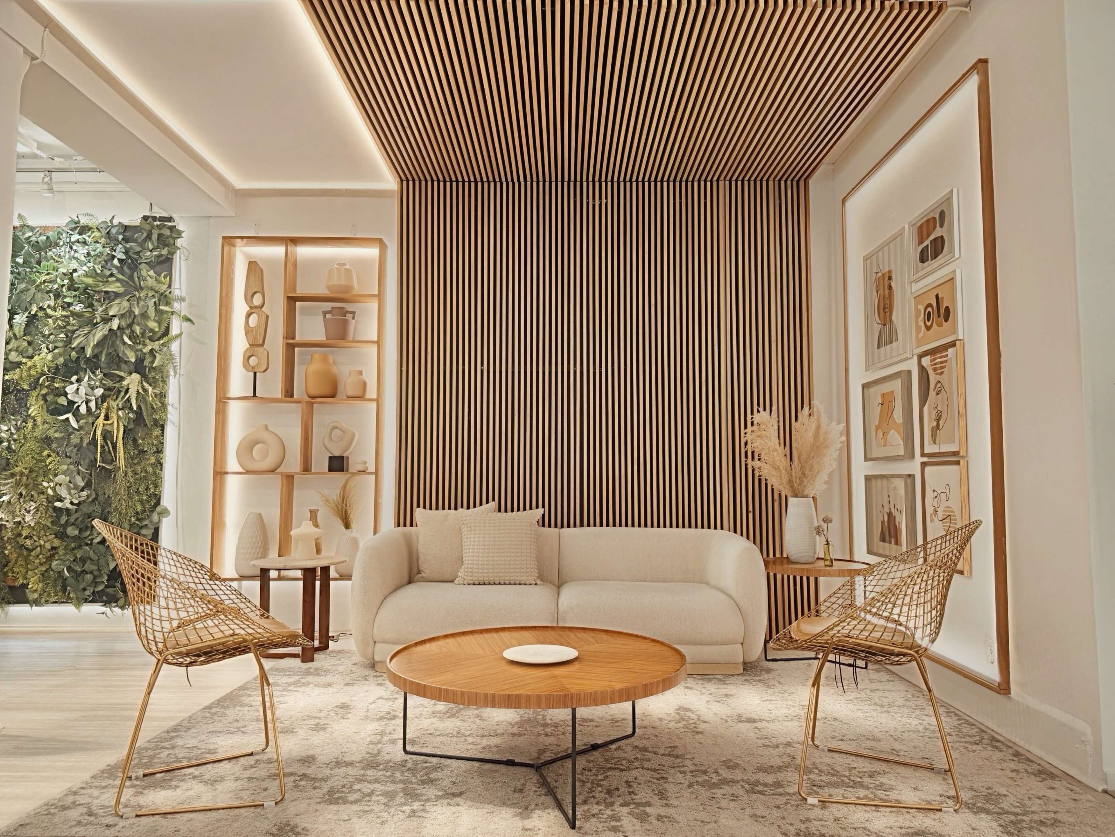 The image features a modern living room with a beige sofa, two wire chairs, a round wooden coffee table, and a wall adorned with vertical wooden slats and decorative shelves.