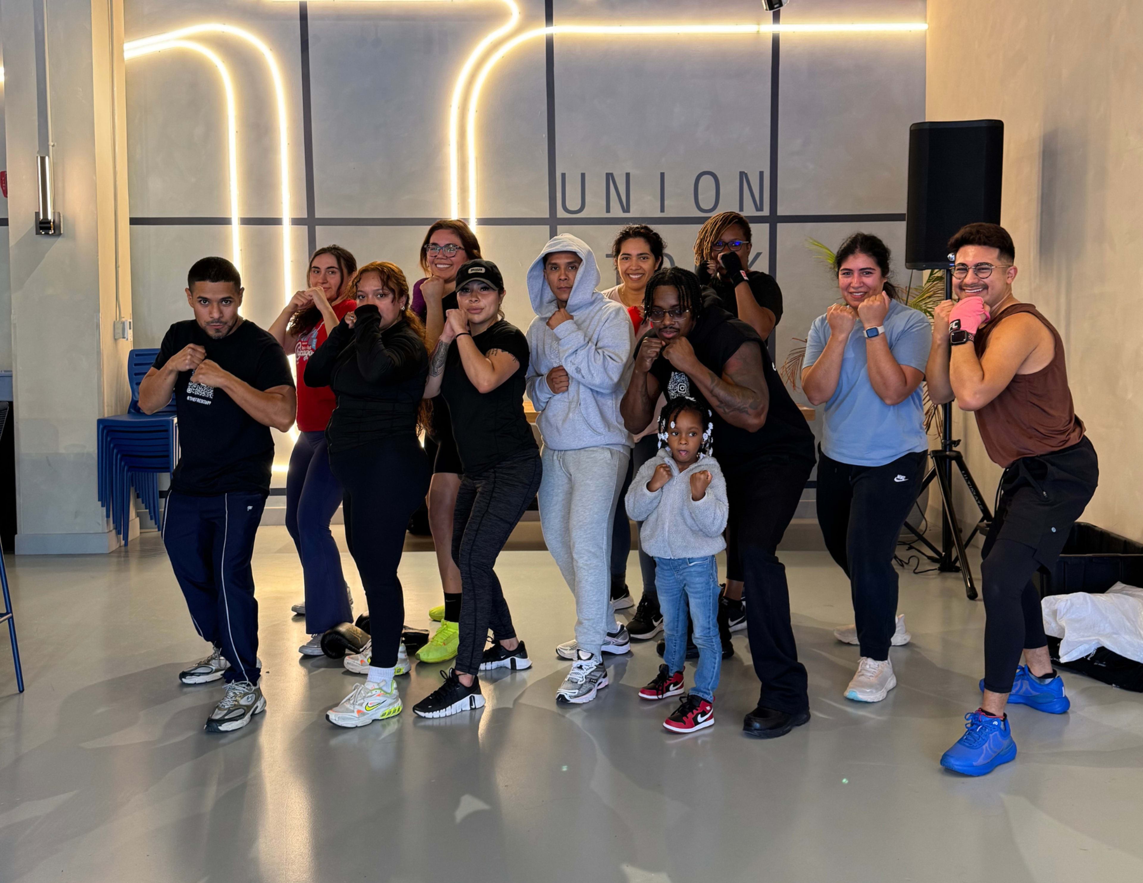 A diverse group of individuals poses in a boxing stance inside a modern studio.
