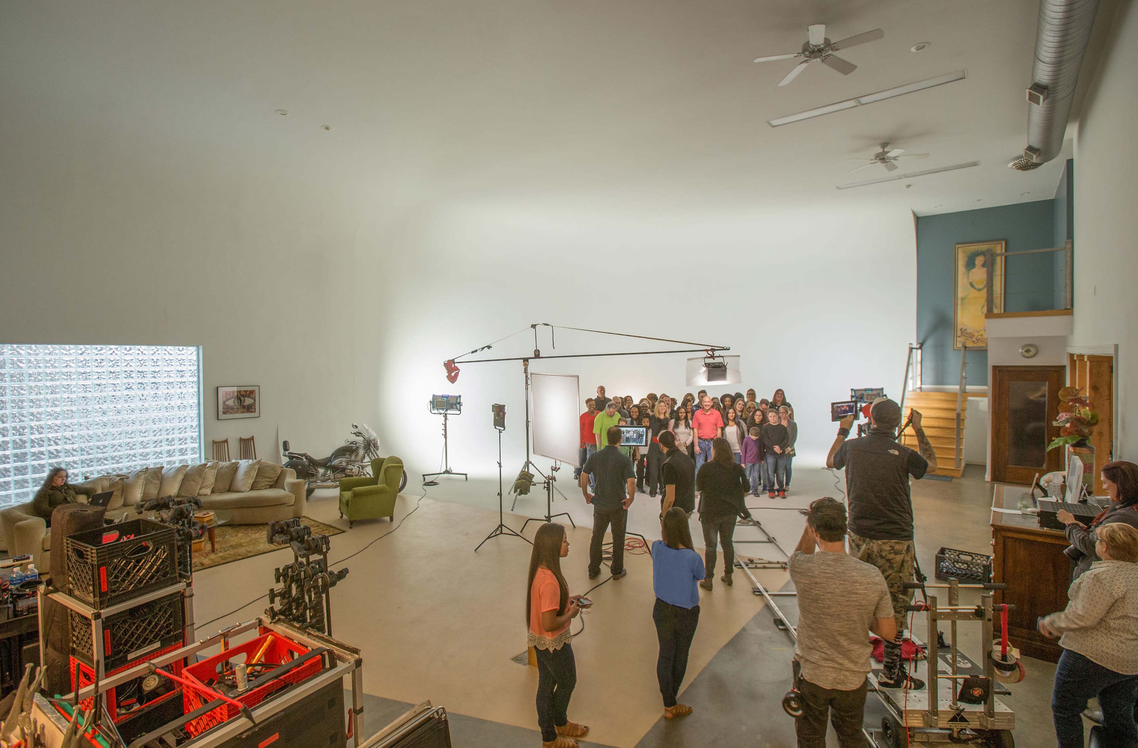 A group of people stands in a well-lit studio surrounded by filming equipment and lighting setups.