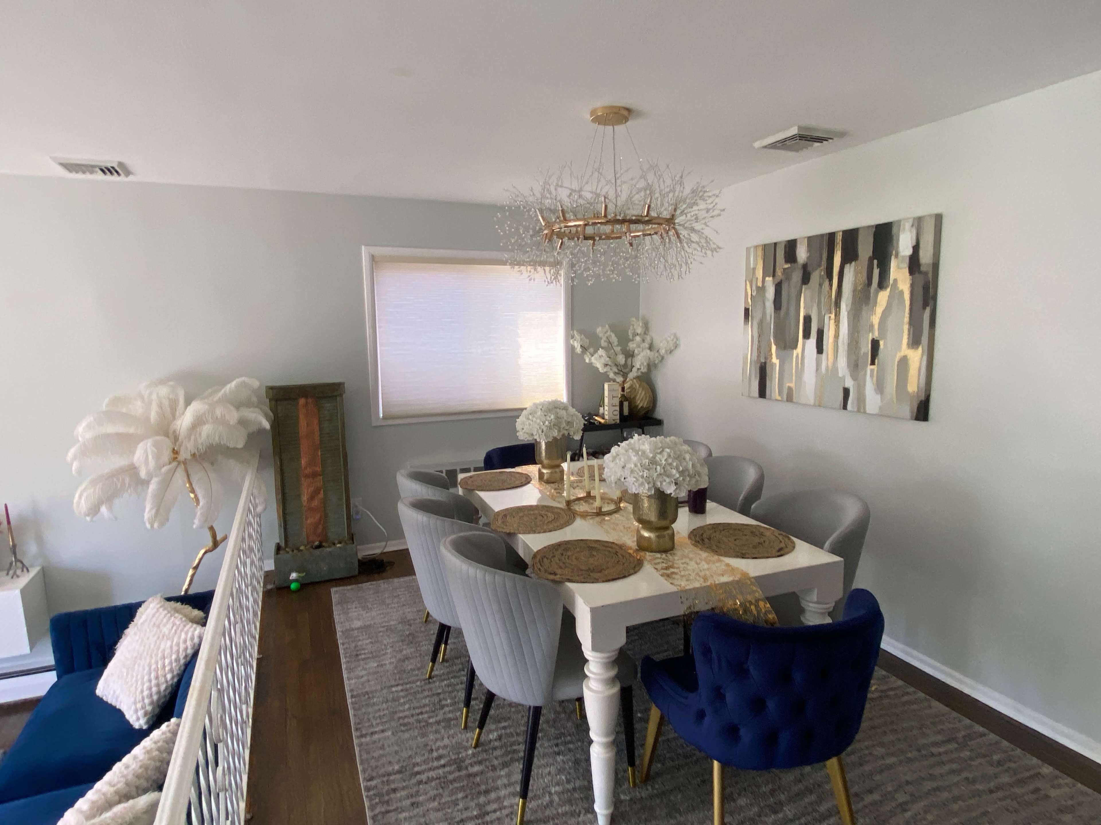 A dining room with a table set for eight, surrounded by upholstered chairs, and a modern chandelier overhead.