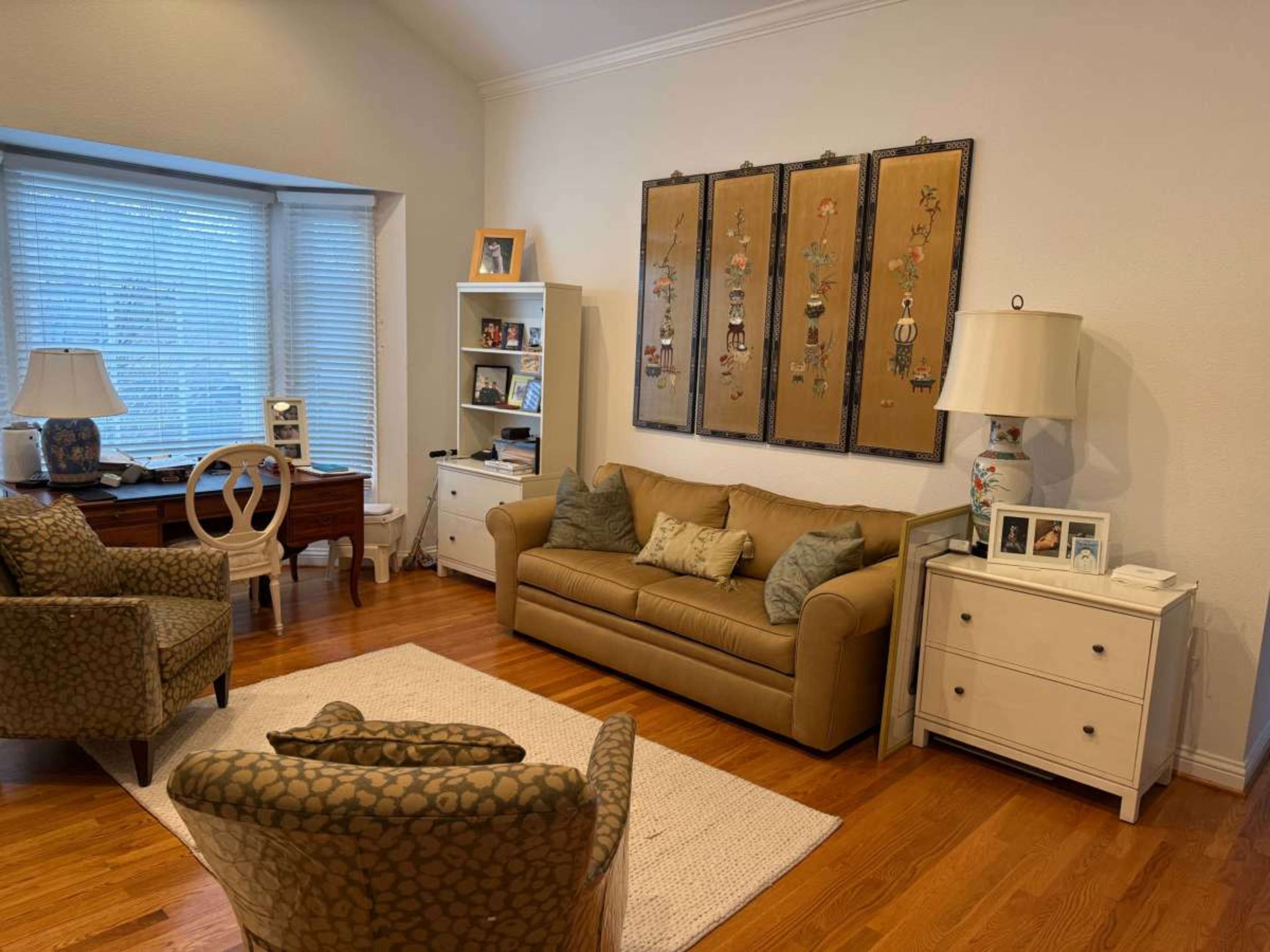 The image shows a cozy living room with a tan couch, two patterned chairs, a coffee table, and framed artwork on the wall.