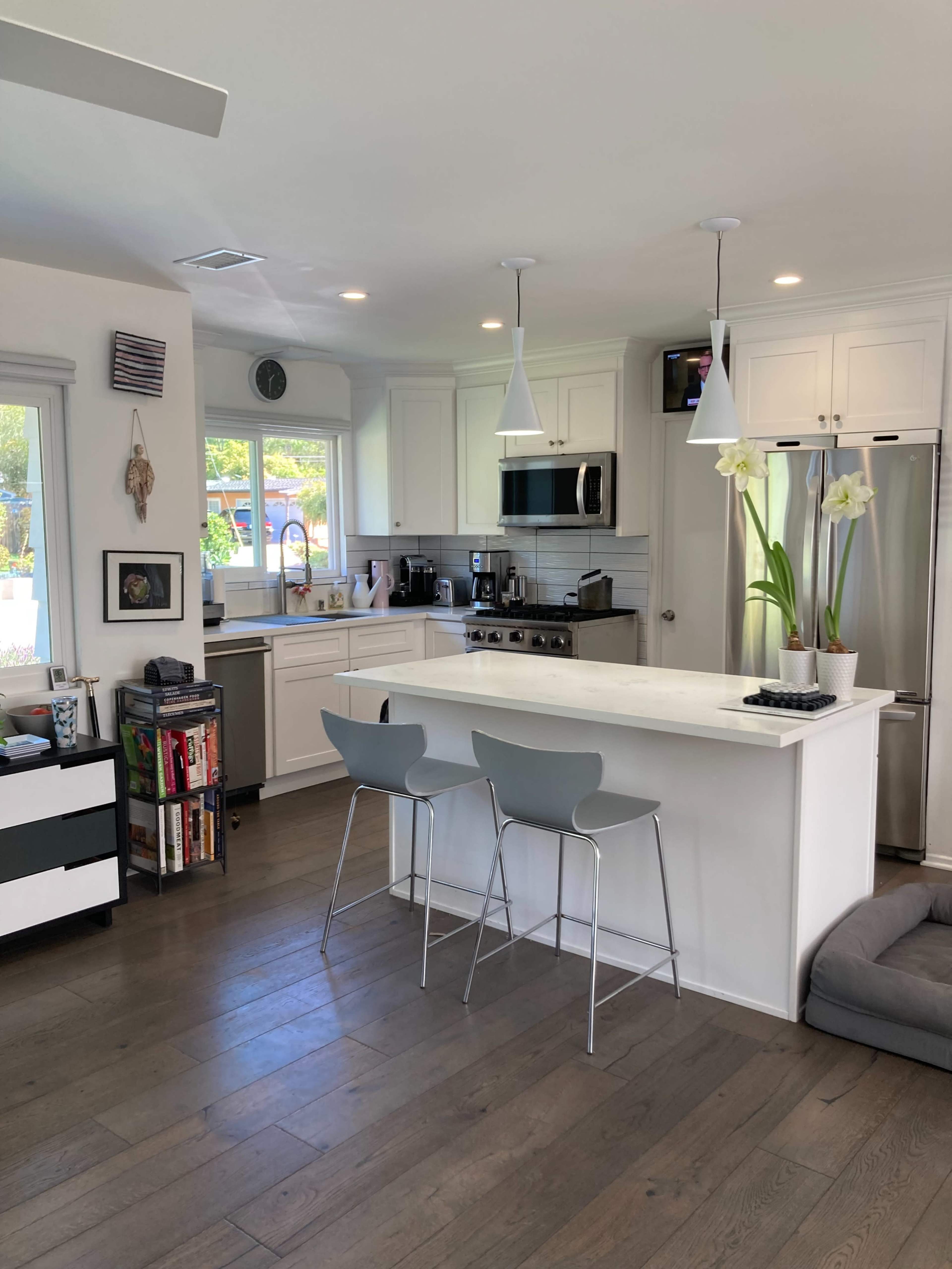 A modern kitchen features white cabinetry, a marble countertop island with two gray stools, and stainless steel appliances.