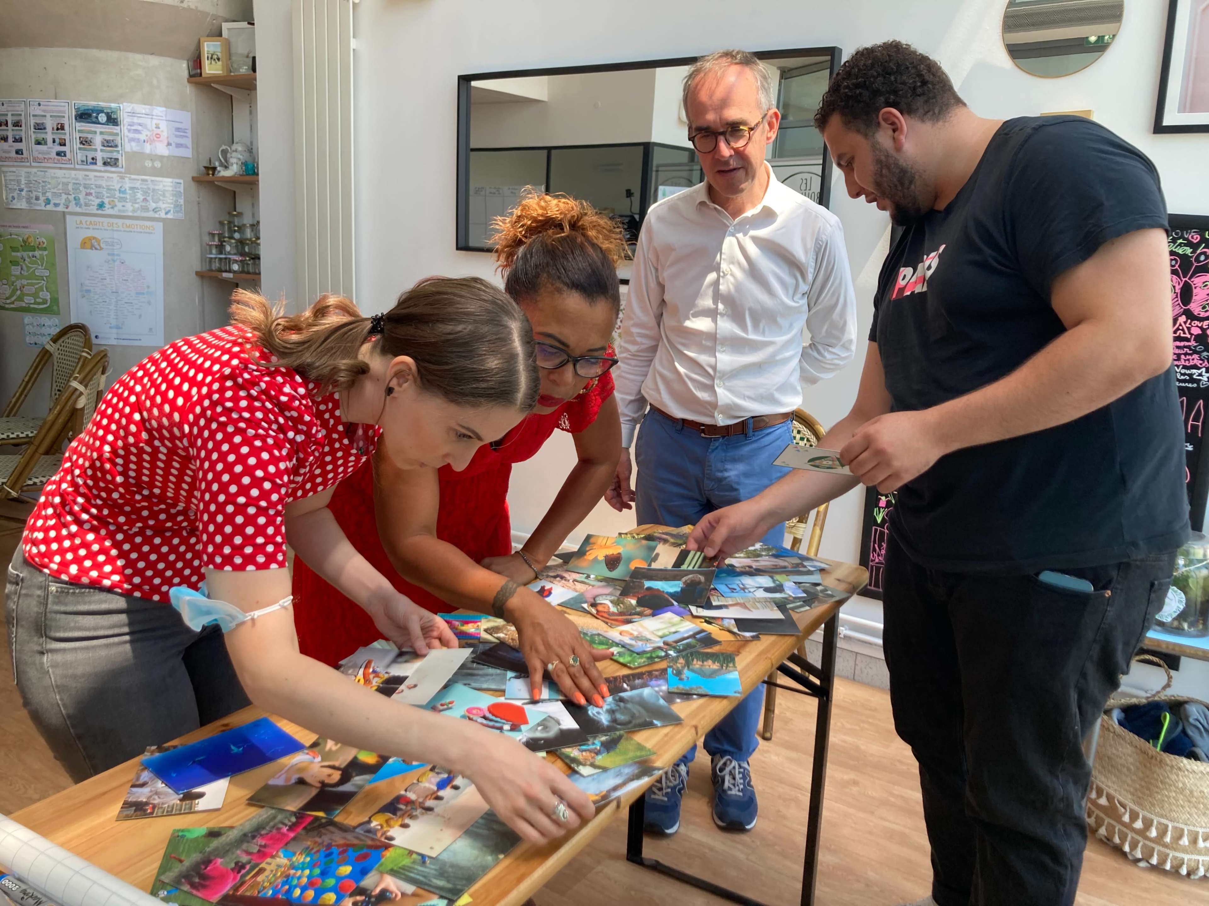 A group of four people is examining a collection of photographs on a table in a bright, decorated room.