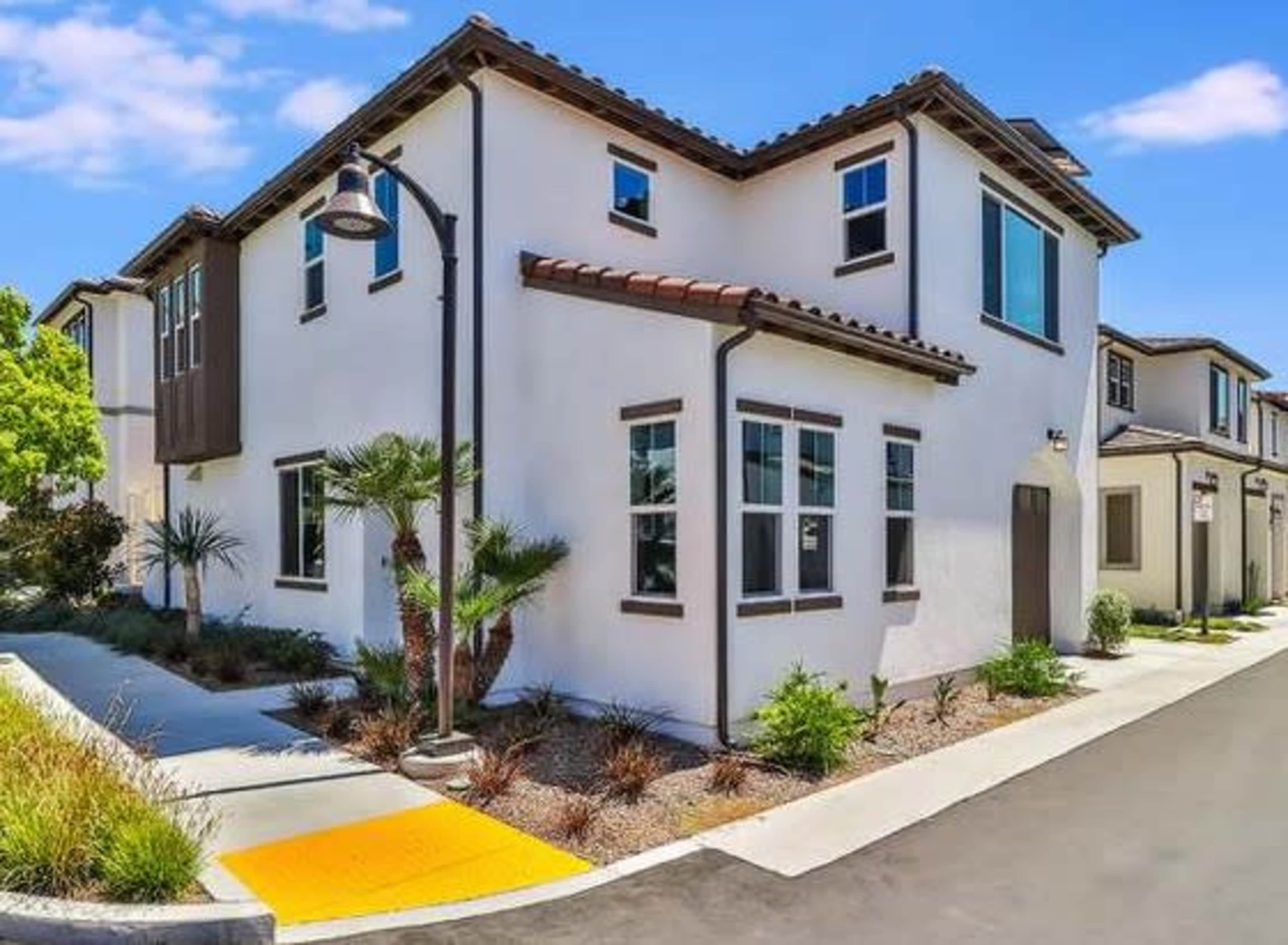 A modern two-story house with white walls, a tiled roof, and landscaping along a walkway and driveway.