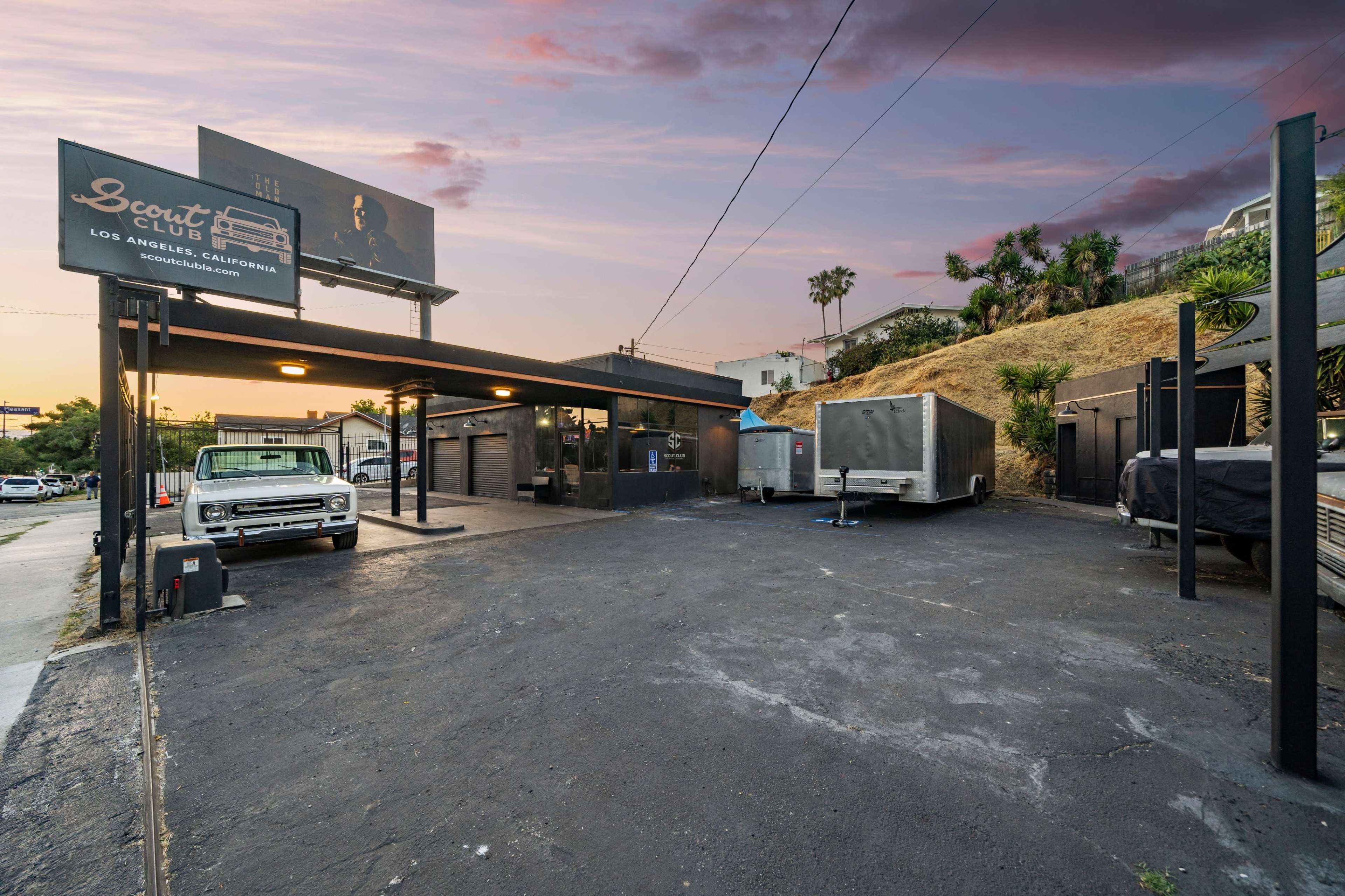 A parking area outside a building labeled "Scout Club" in Los Angeles, California, with several trailers and a vintage pickup truck parked nearby.