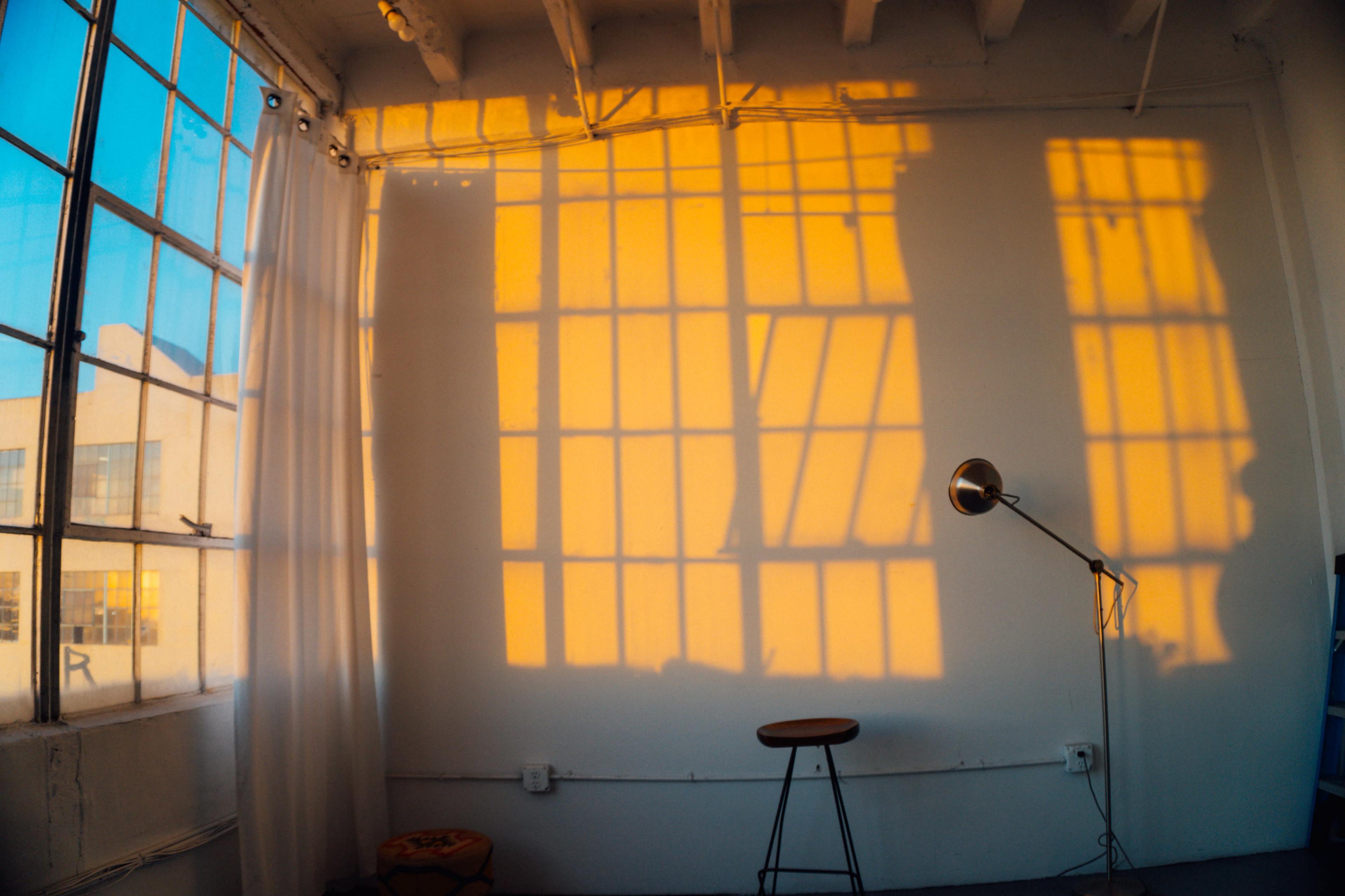 The image shows a sunlit room with large windows, where shadows from the window frames create patterns on the wall and floor.
