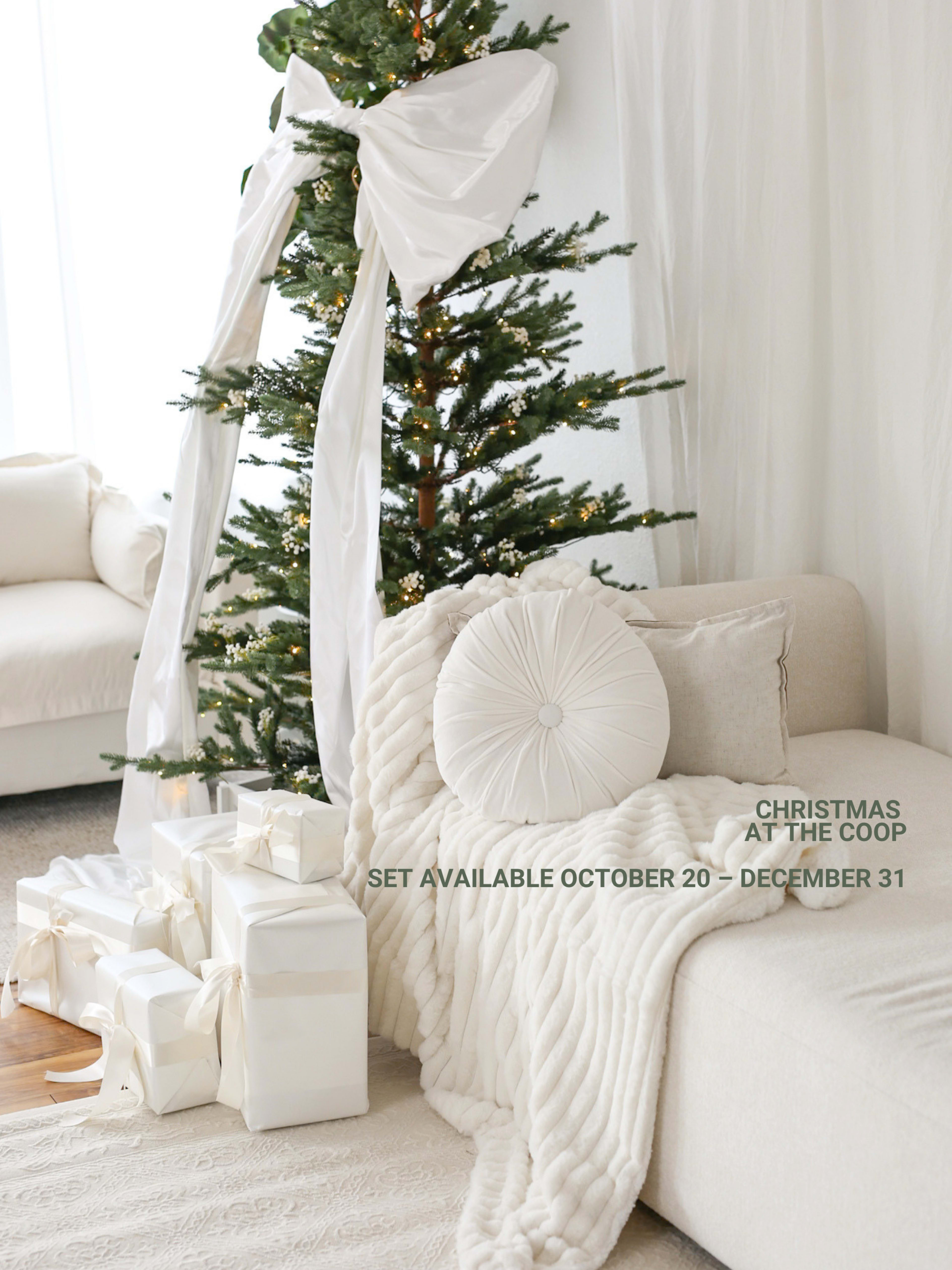 A decorated Christmas tree stands next to a beige couch adorned with a white blanket and pillows, with wrapped gifts placed at the base of the tree.