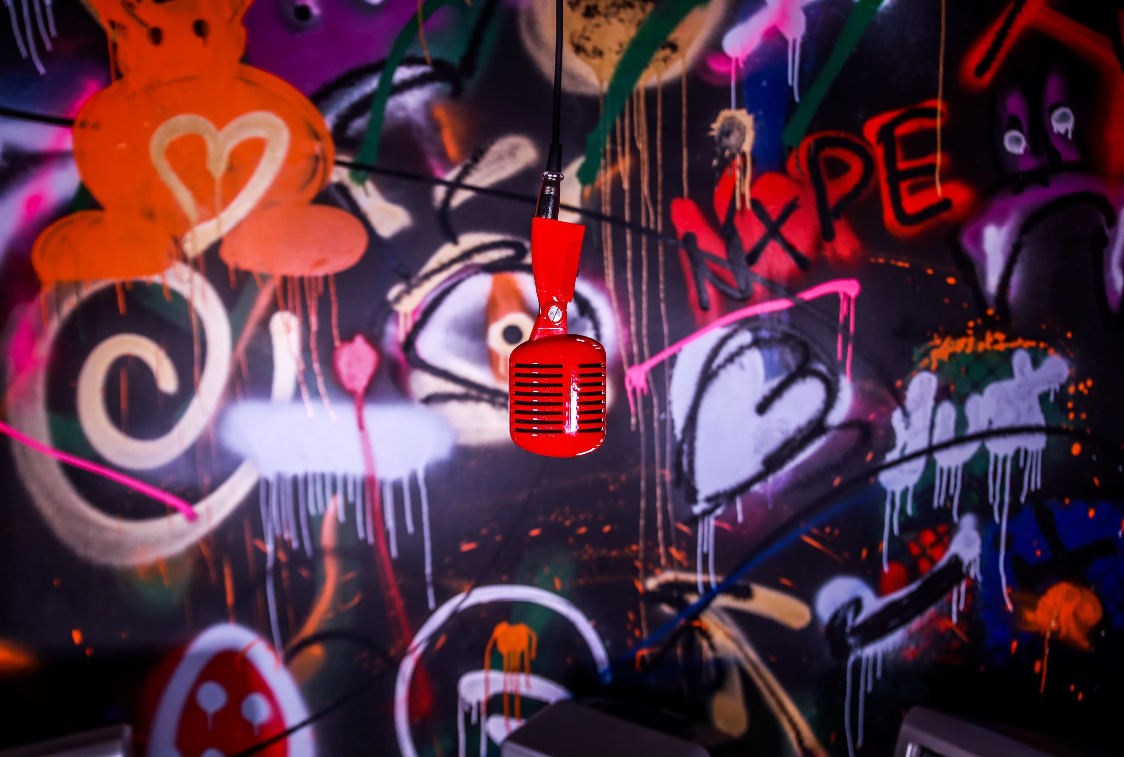 A red vintage microphone hangs in front of a graffiti-covered wall filled with colorful spray paint designs.