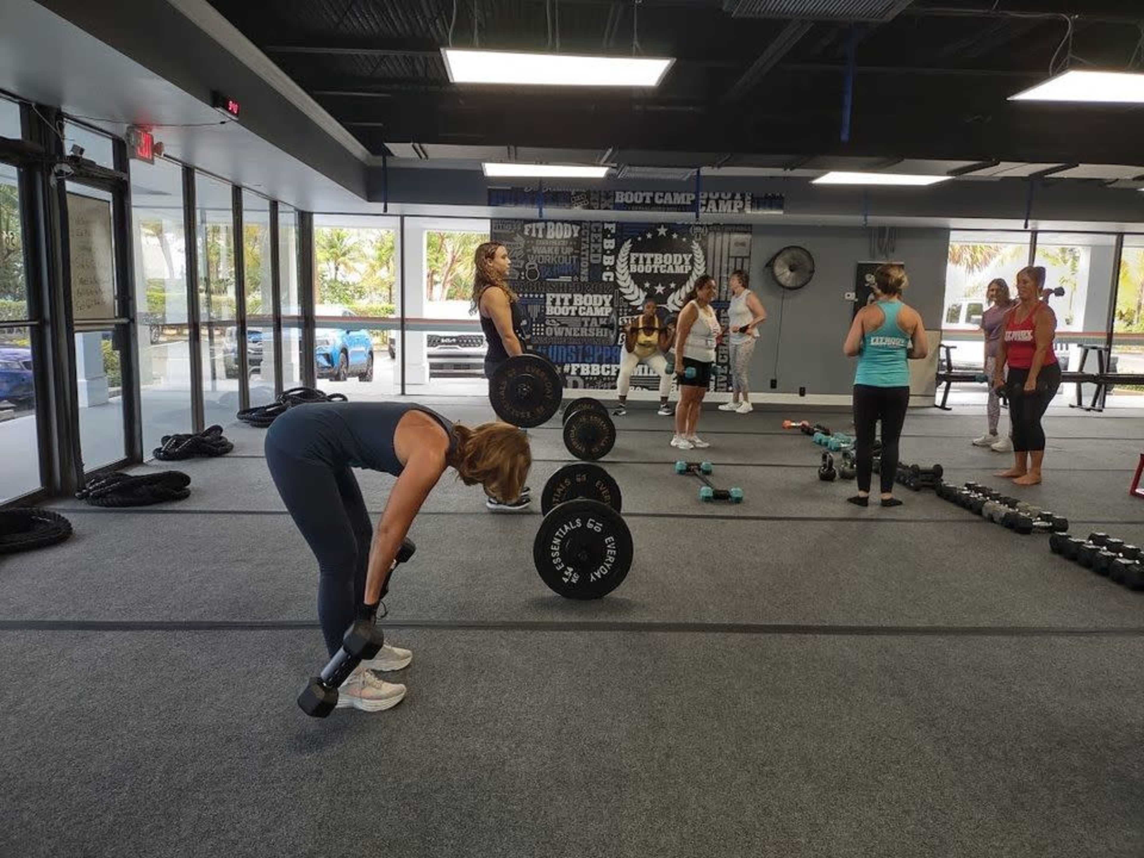 A group of people are engaged in a weightlifting workout in a gym, with some using dumbbells and others preparing for exercises.