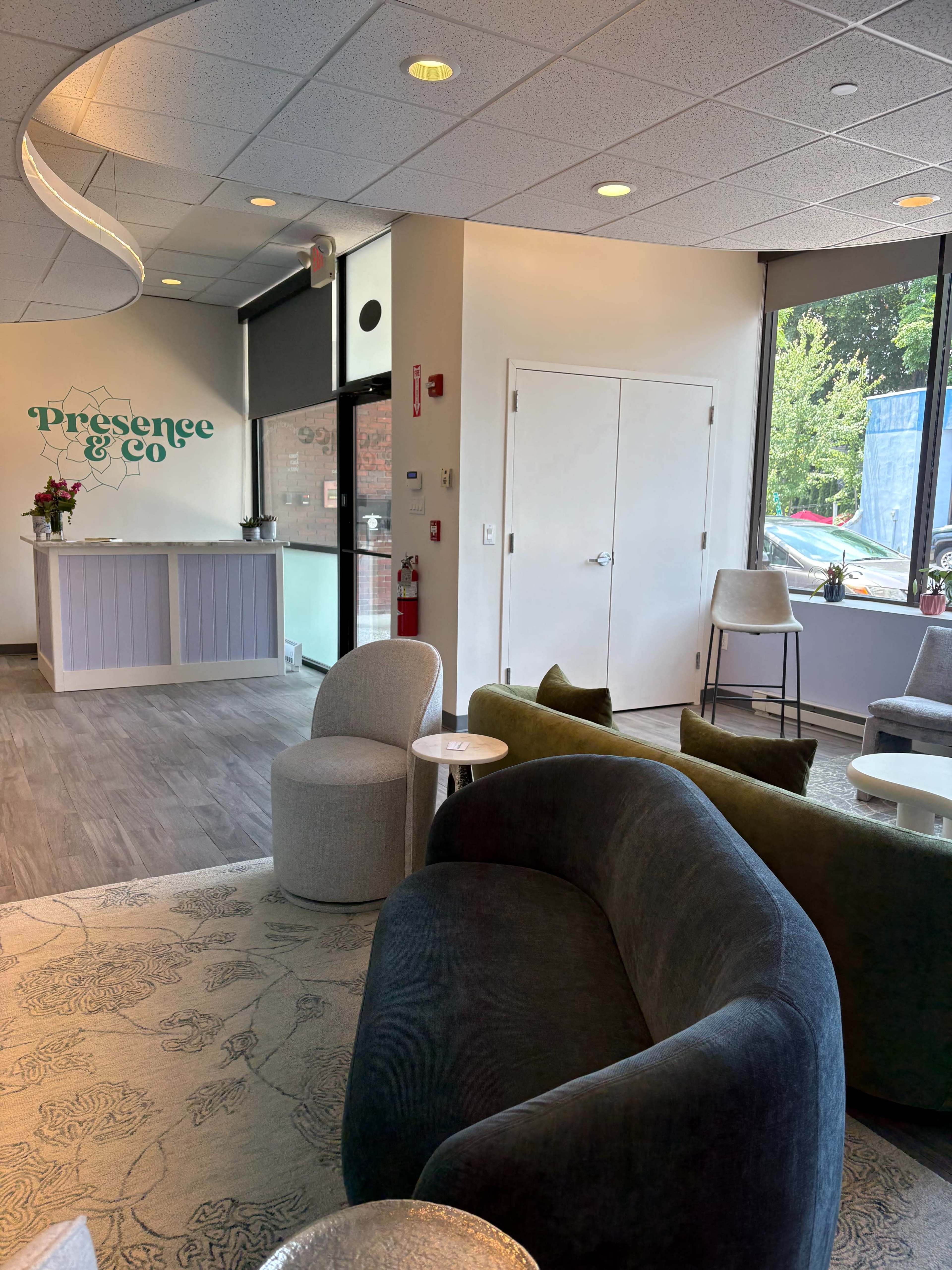The image shows a modern reception area with a curved sofa, small tables, and a reception desk adorned with a floral design.