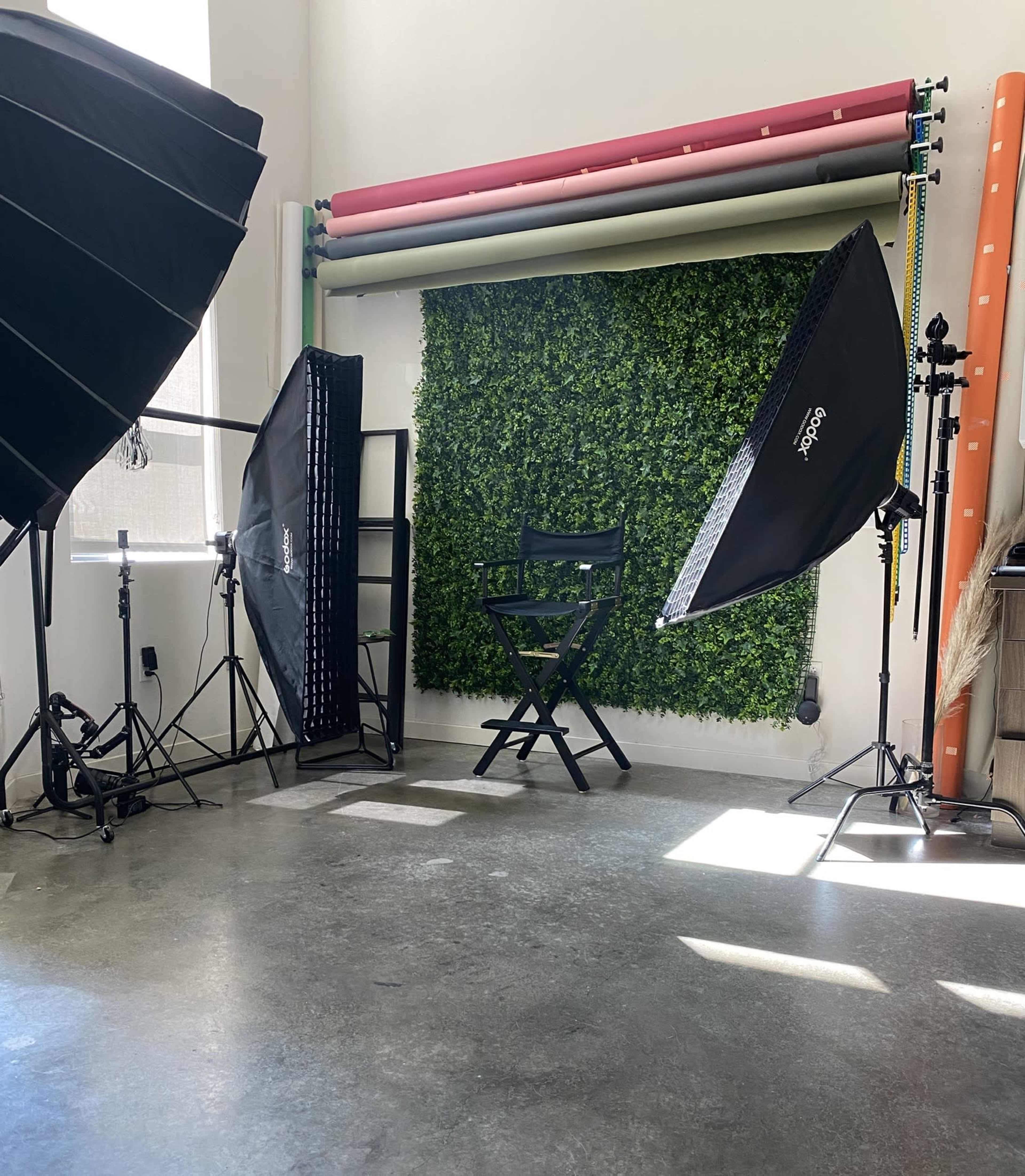 A photography studio setup with backdrops, lighting equipment, and an empty director's chair against a green wall.