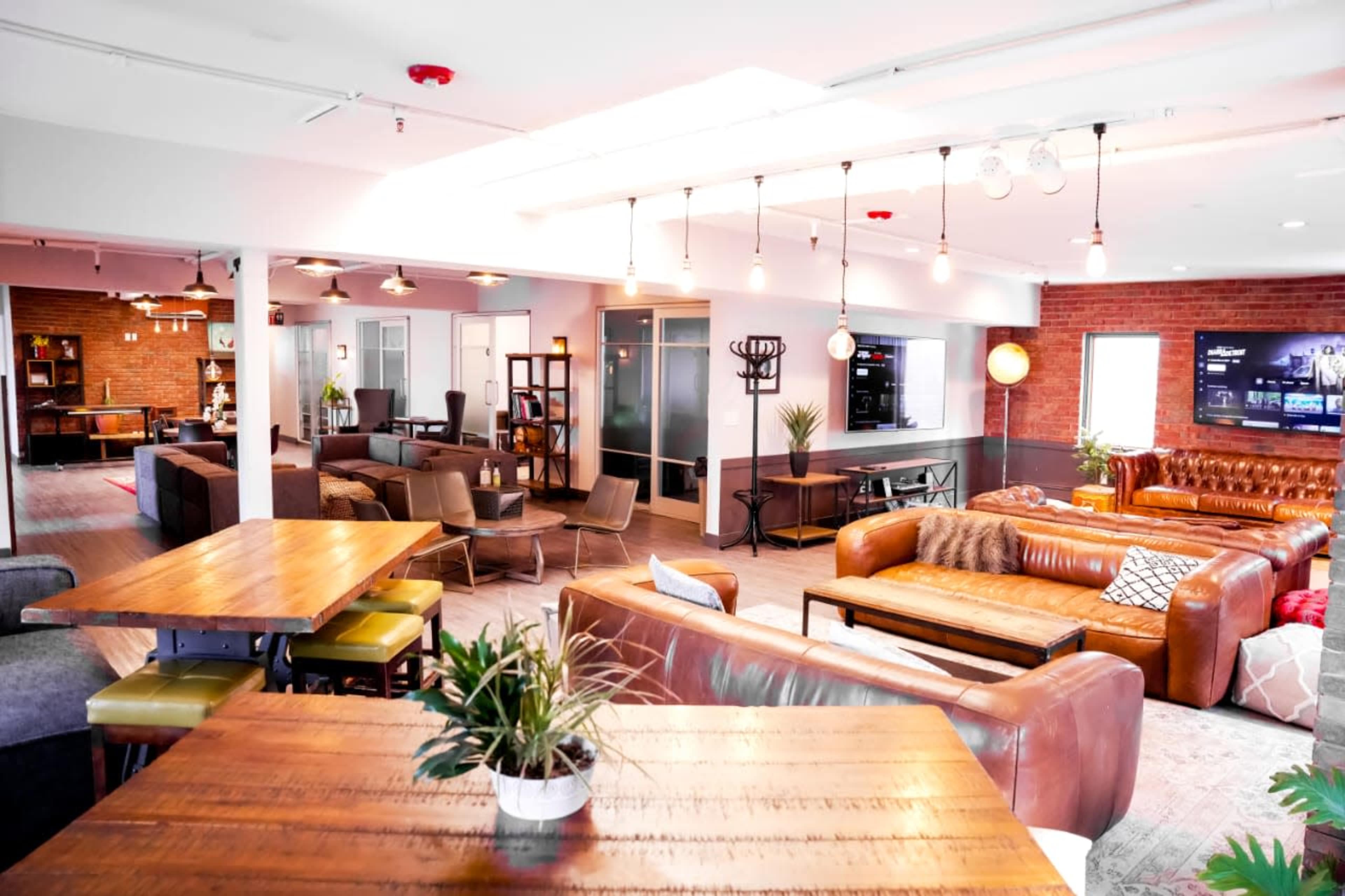 A modern, open office space with various seating areas, wooden tables, and a mix of leather sofas and chairs.