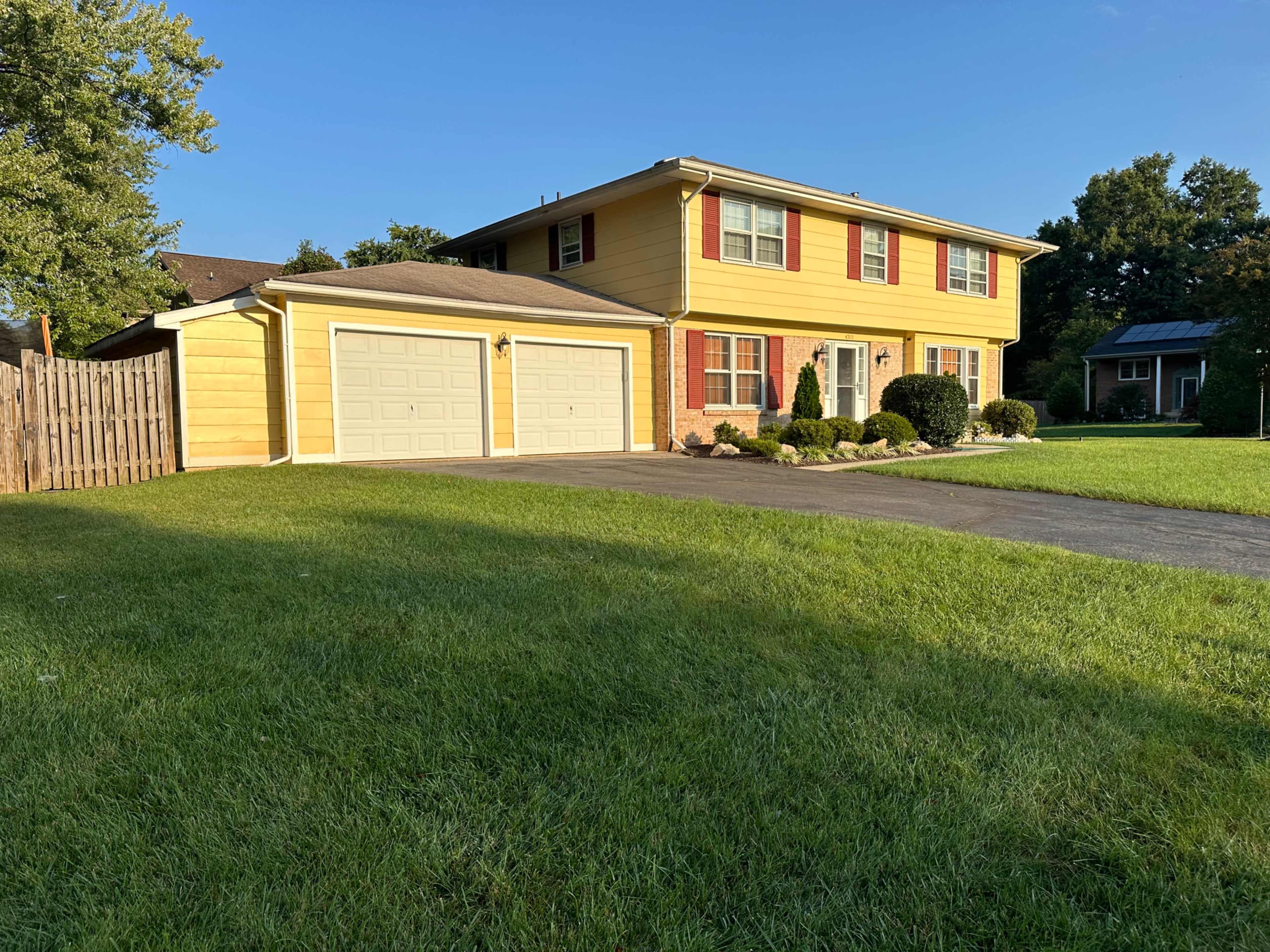 The image shows a two-story yellow house with a double garage and a well-manicured lawn.