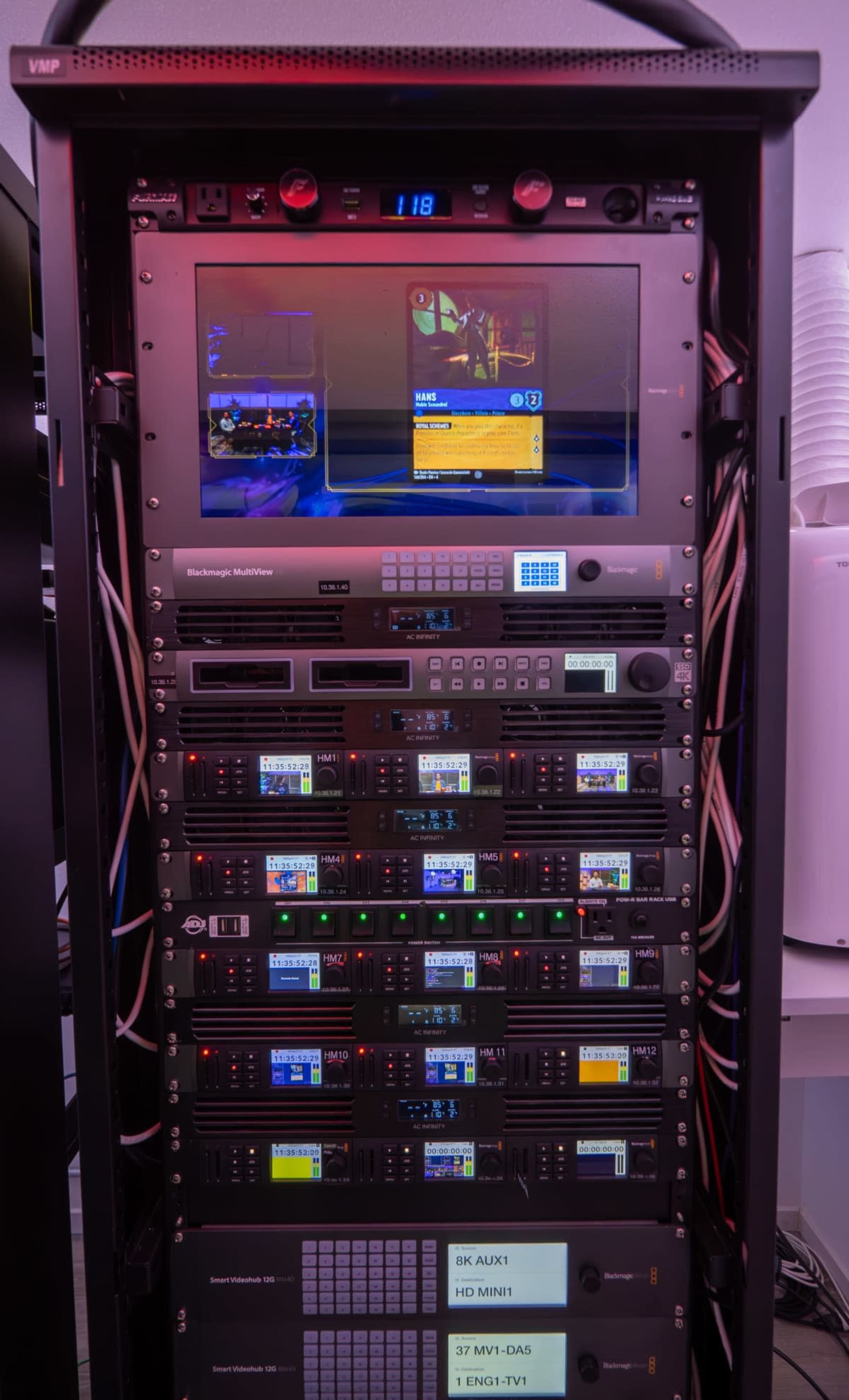 The image shows a rack-mounted server system with multiple devices, including screens, controls, and wiring.