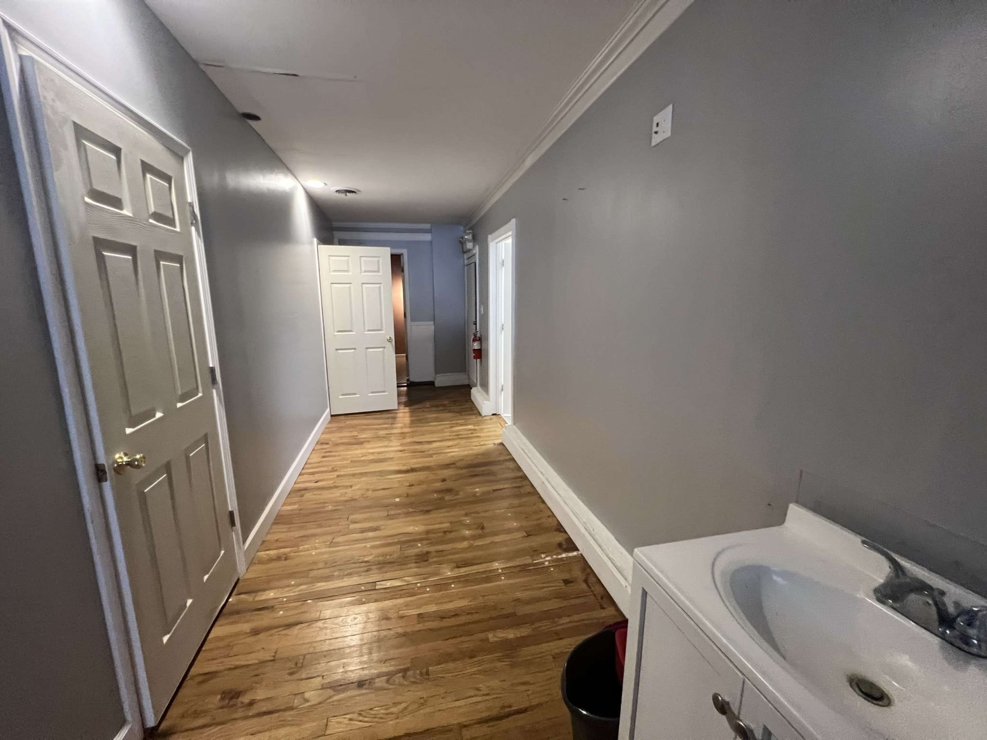 A long hallway with wooden floors, gray walls, and a sink on the right side.