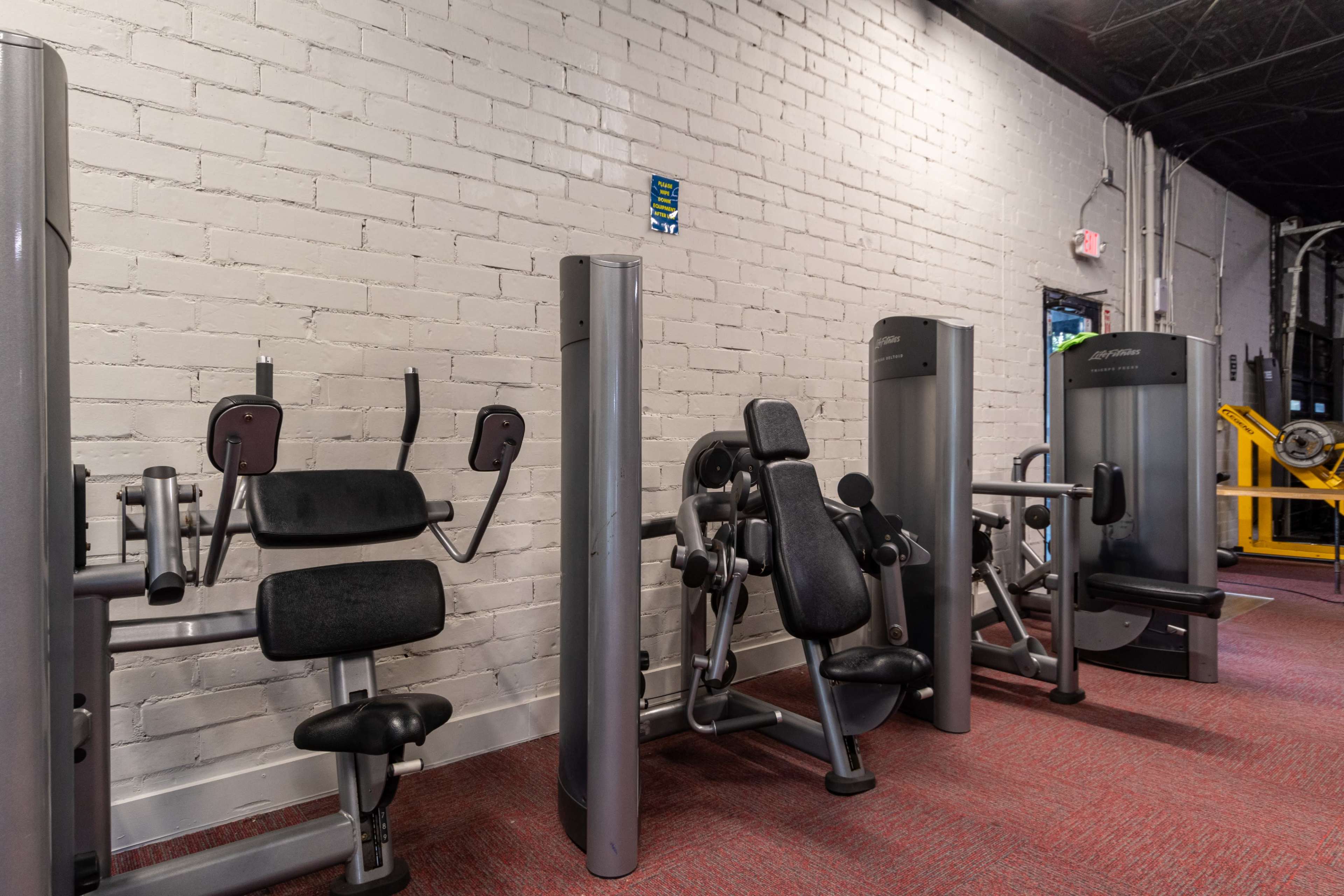 A fitness area with various grey weight machines aligned against a white brick wall.