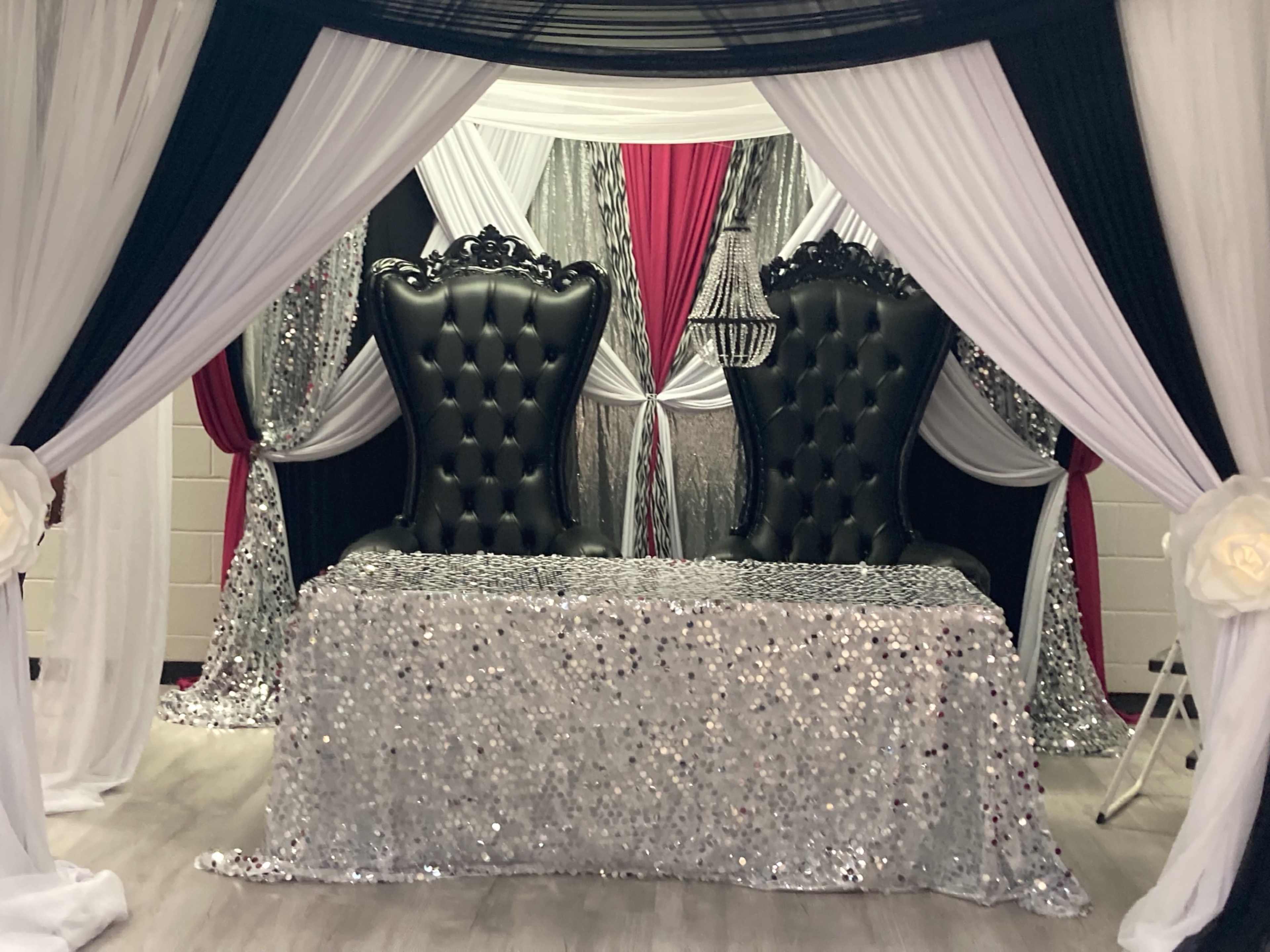 A decorative seating area featuring two large black tufted chairs under a draped canopy with silver and black accents.