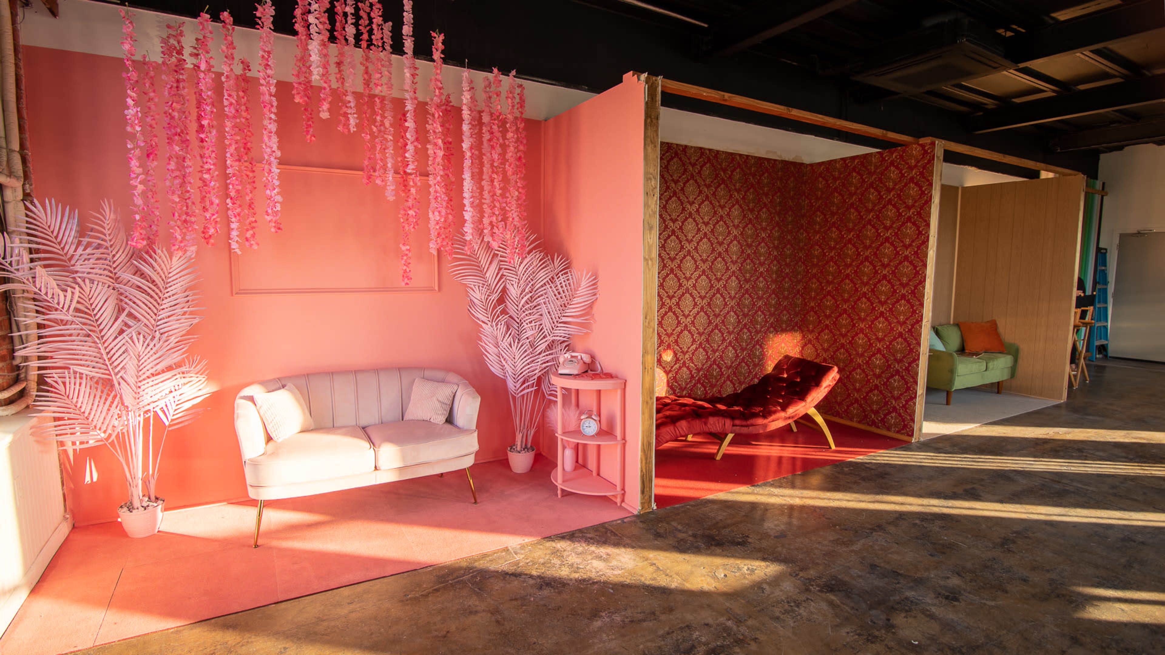 A colorful interior space with pink and red walls, a plush sofa, decorative plants, and various furniture arrangements.