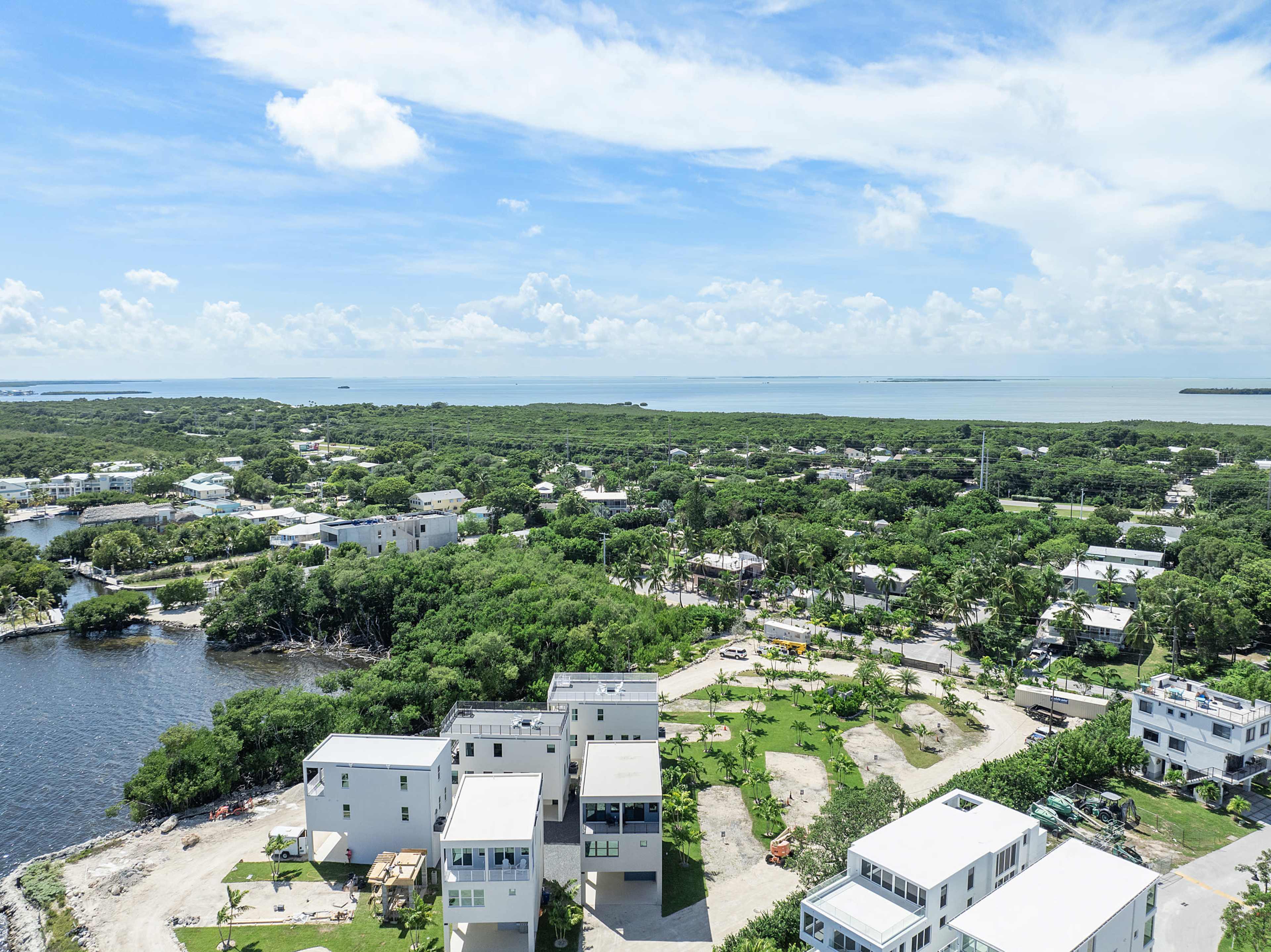 The image shows a coastal area with several modern houses, greenery, and a body of water visible in the background.