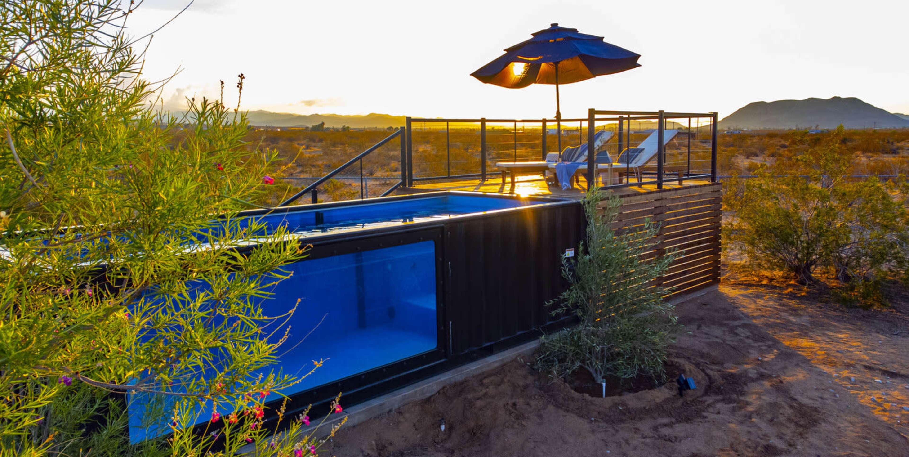 A shipping container is transformed into a modern living space with a pool and a deck, set against a desert landscape at sunset.