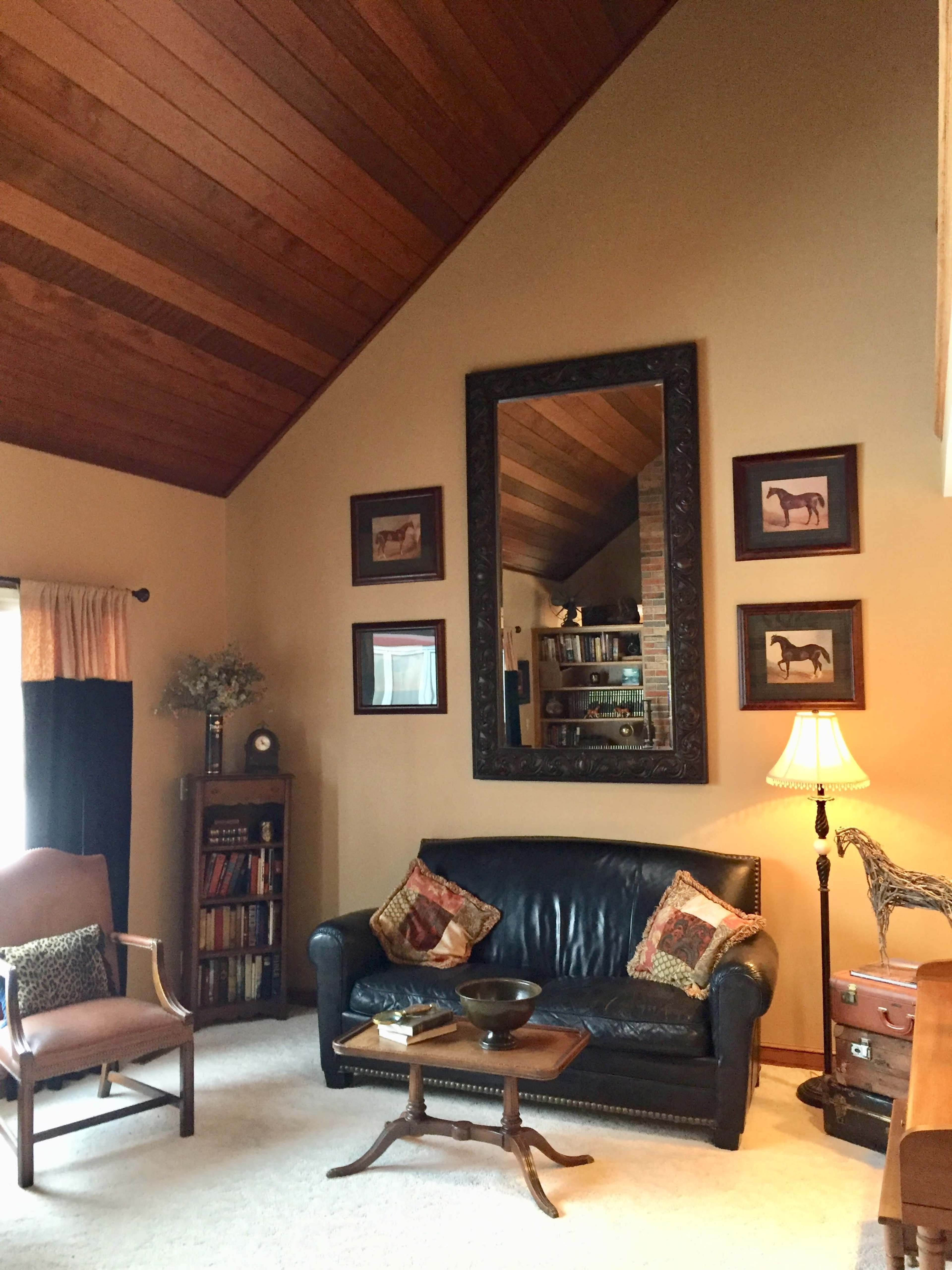 A living room with a leather sofa, a wooden ceiling, framed horse prints on the walls, and a lamp next to a chair.