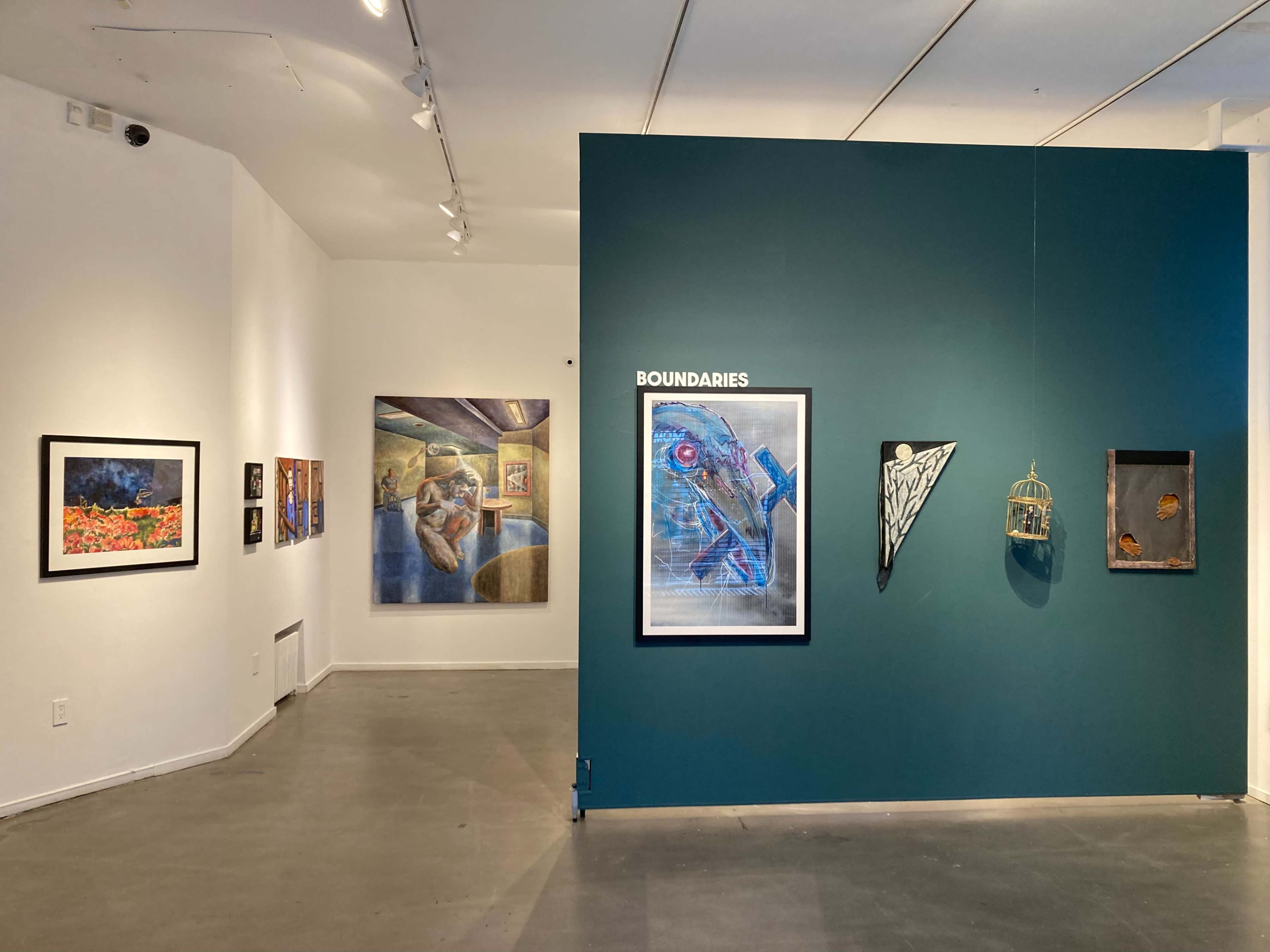 The image shows an art gallery featuring framed artworks on white walls and a green accent wall displaying various pieces, including a work titled "Boundaries."