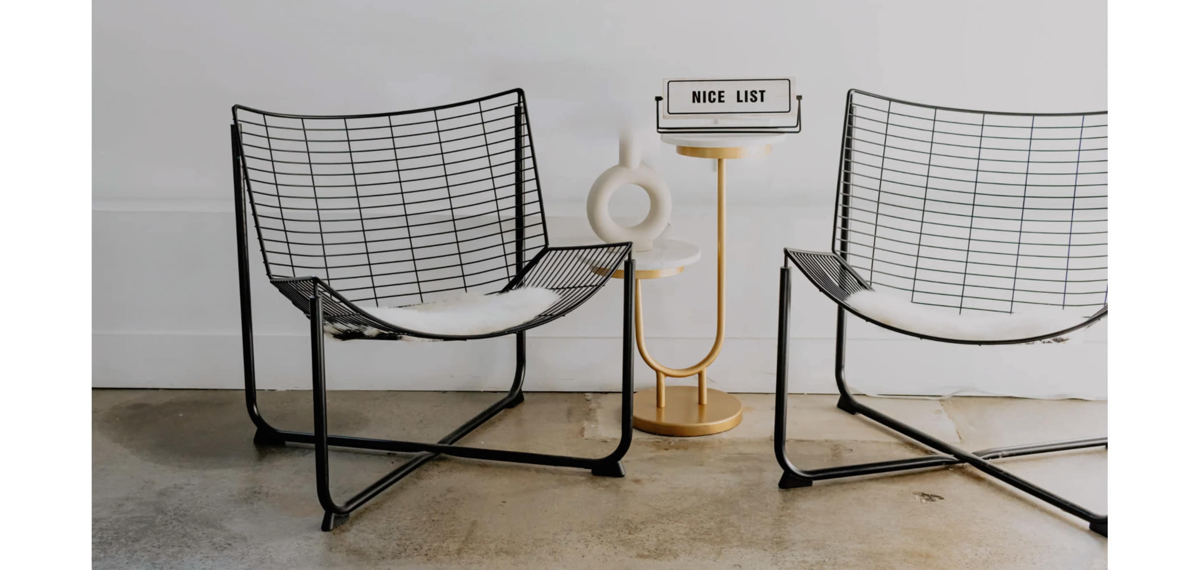 Two wire-frame lounge chairs are positioned beside a small, round table holding a sign that reads "NICE LIST."