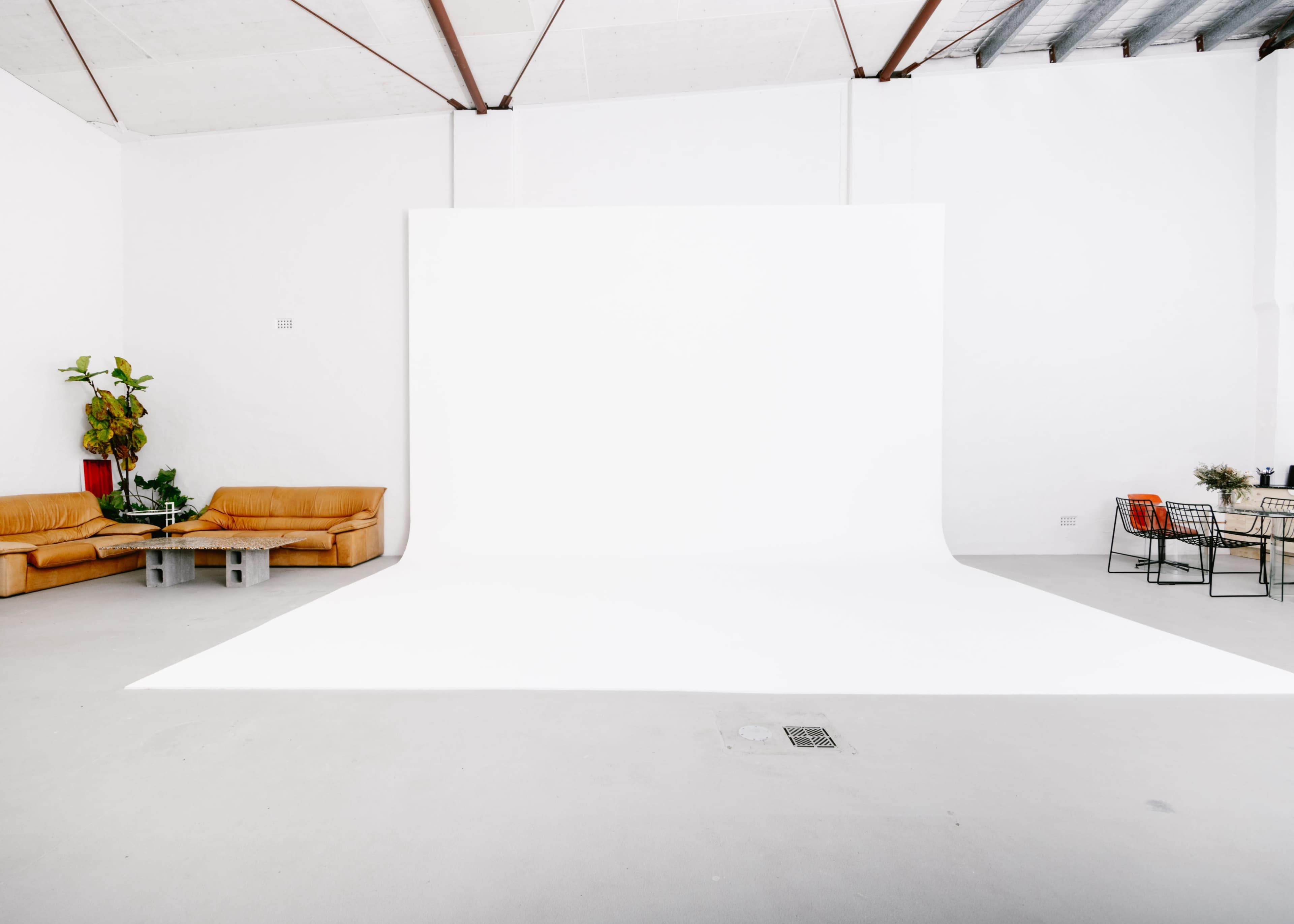 A spacious, minimalist studio with a white backdrop, two tan couches, and a small table surrounded by metal chairs.
