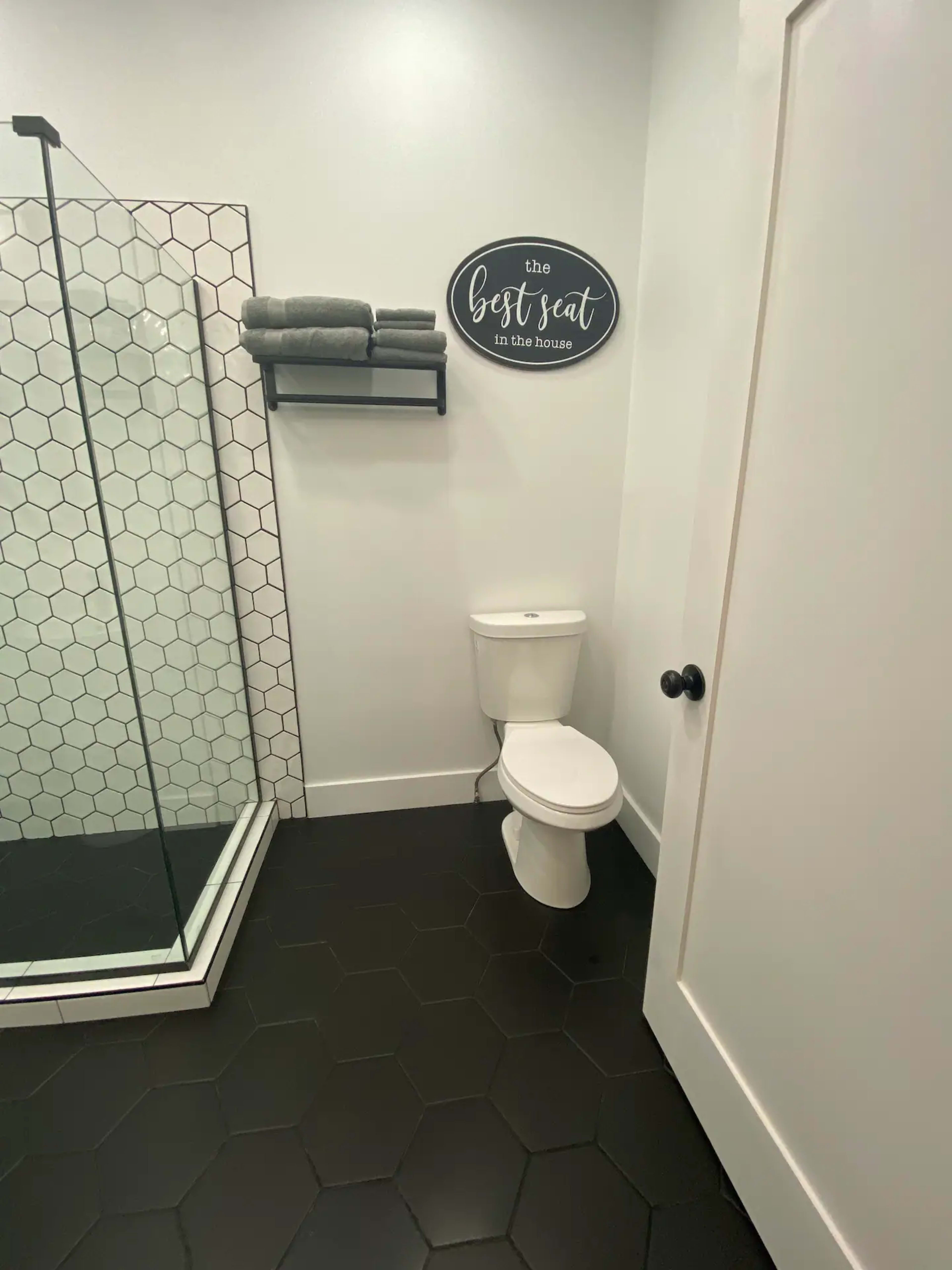 A modern bathroom featuring a glass shower, a toilet, and a sign on the wall that reads "the best seat in the house."