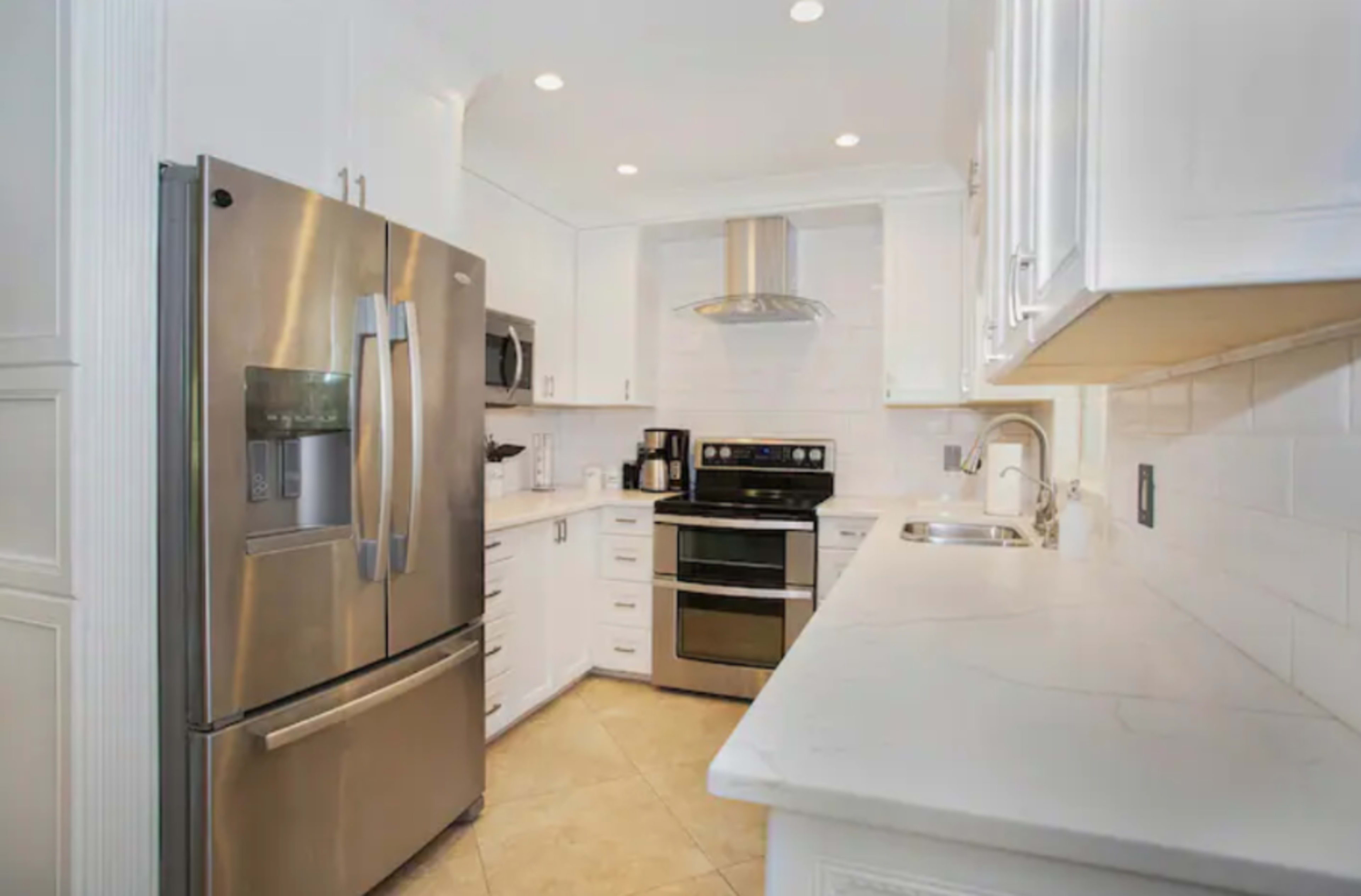 A modern kitchen features stainless steel appliances, white cabinetry, and a marble countertop.