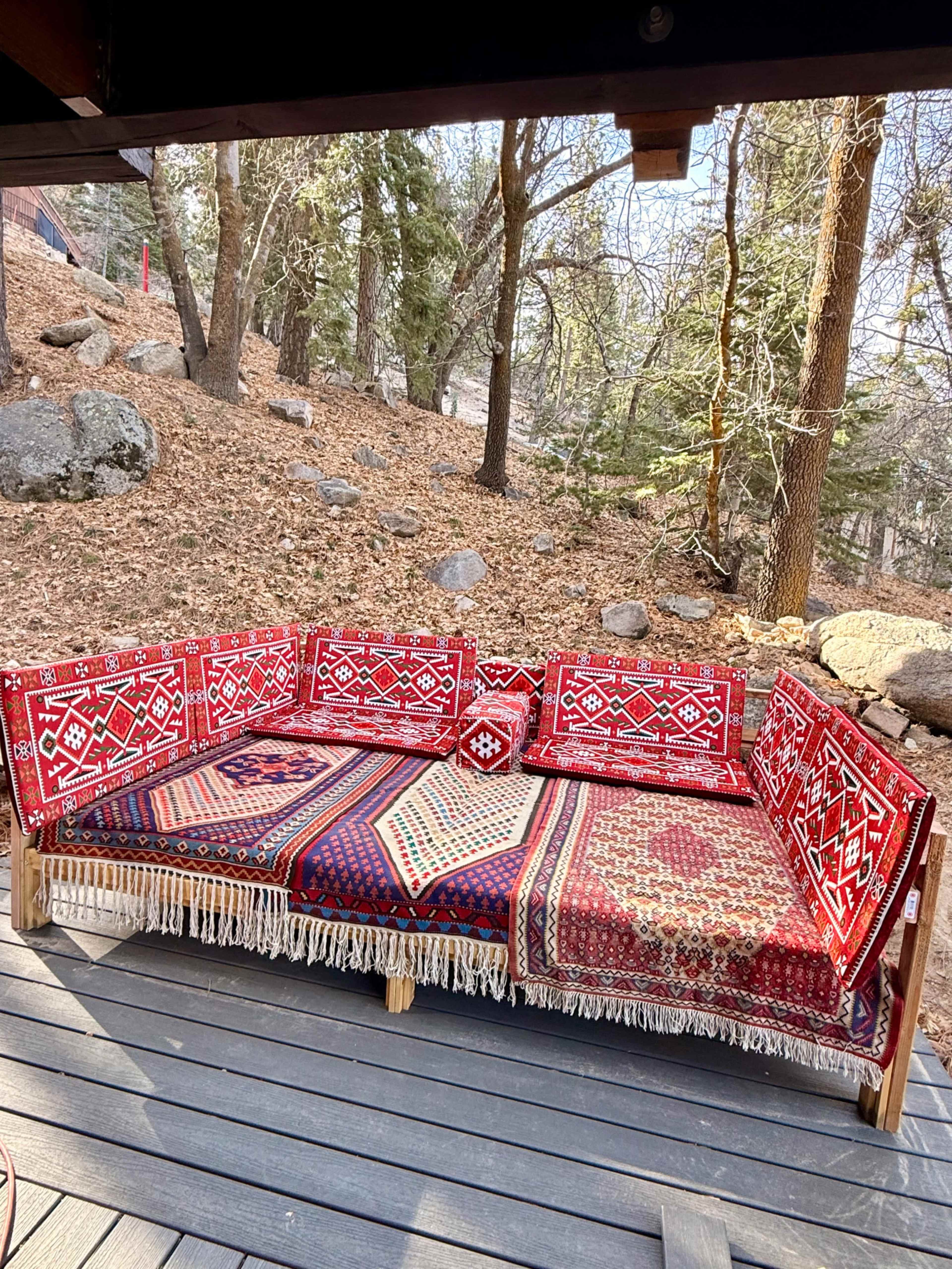 A cozy seating area is adorned with colorful patterned textiles, set against a backdrop of trees and a leaf-covered ground.