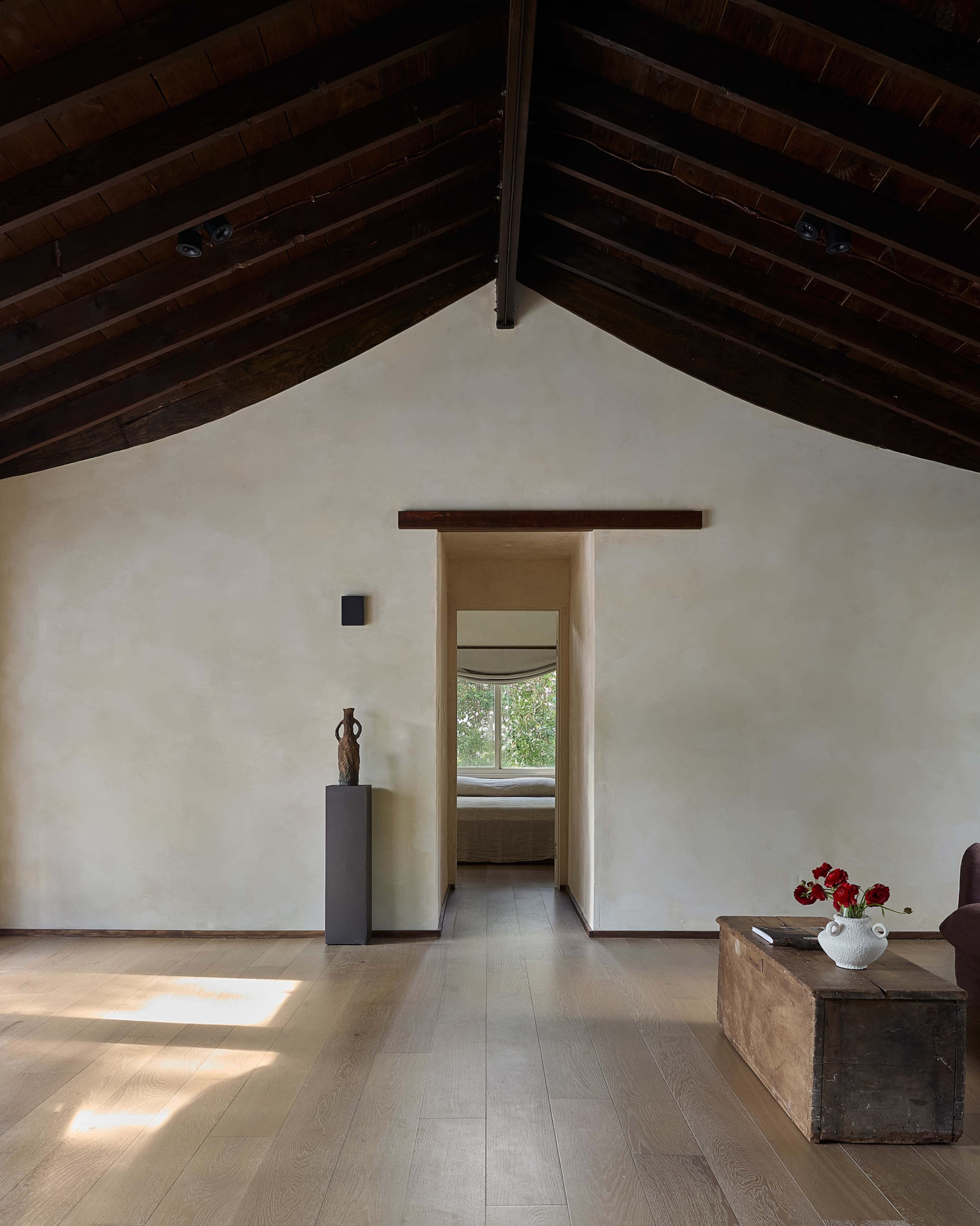 A spacious interior features a high, sloped wooden ceiling, a doorway leading to another room, and a small table with flowers in front of a window.