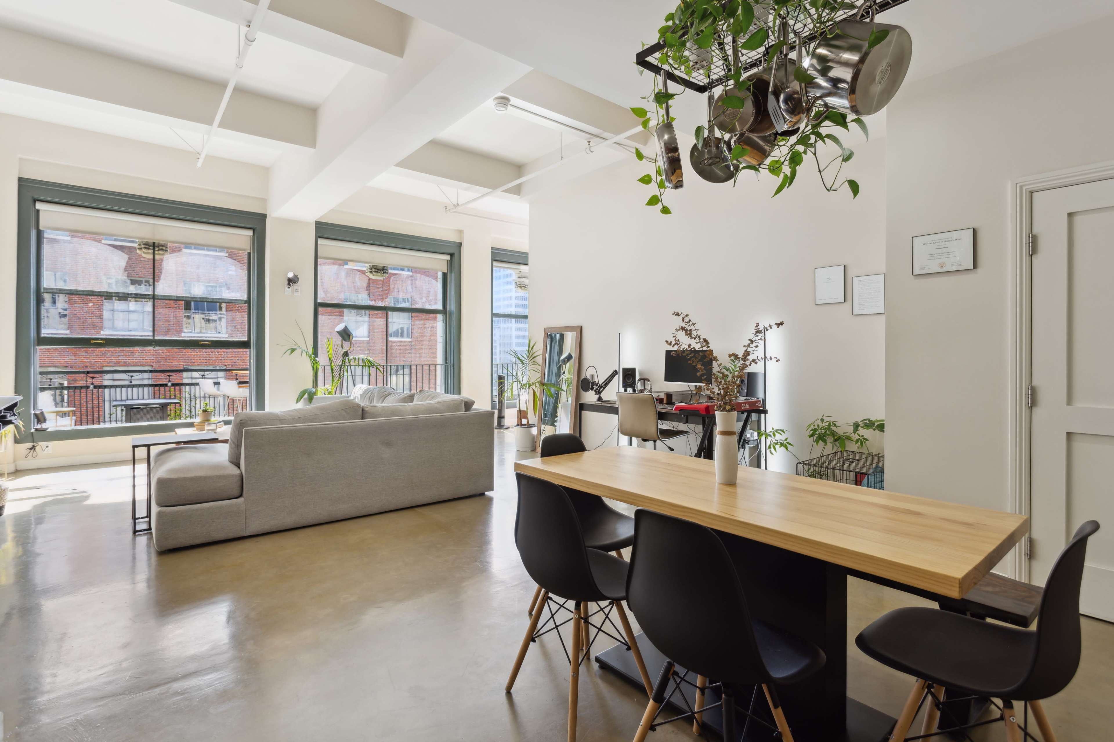 A modern, open-concept living space with a dining table, black chairs, a sofa, and large windows allowing natural light to fill the room.