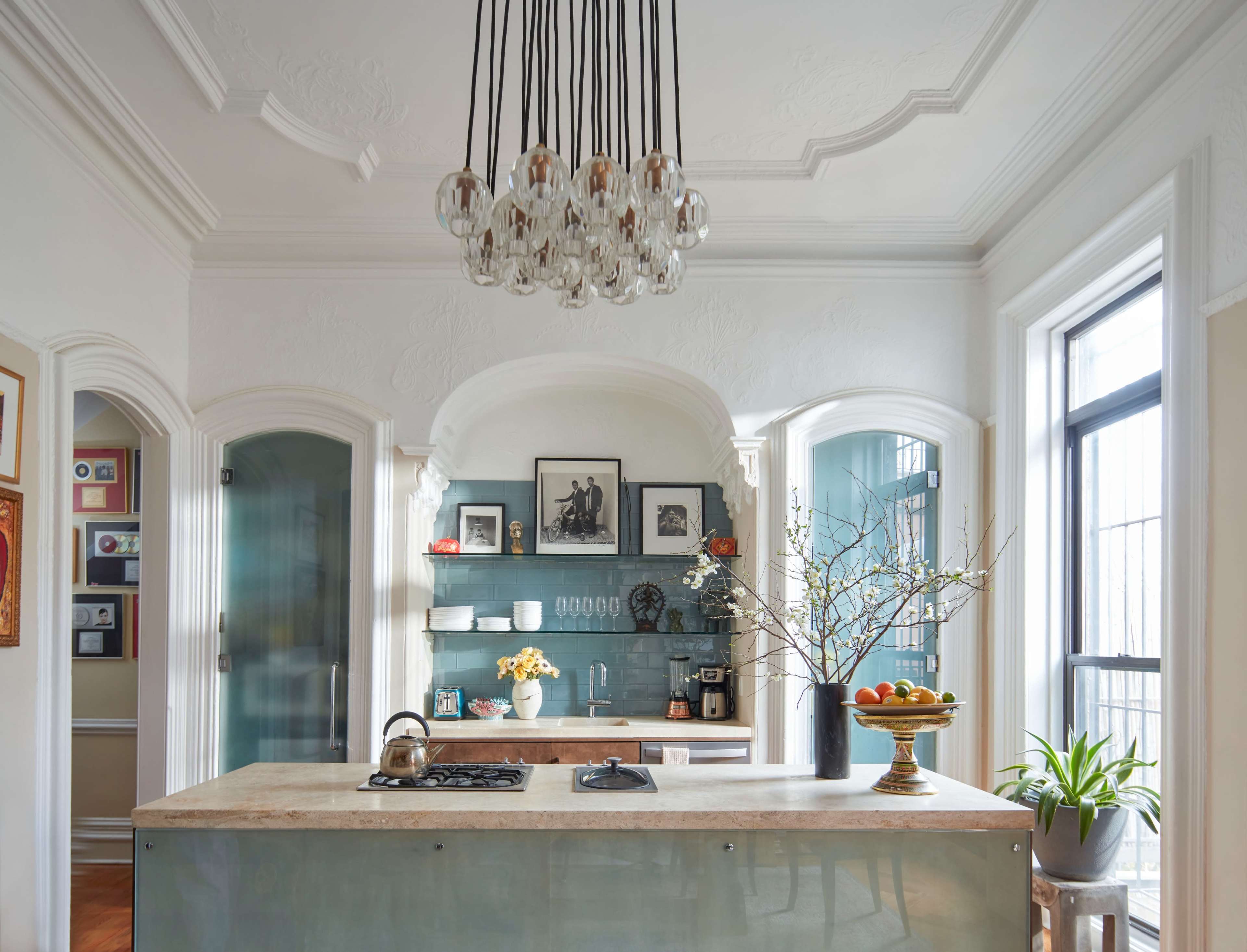 A modern kitchen featuring an island with a gas stove, a decorative light fixture above, and blue tiled walls adorned with framed photos and a vase of flowers.