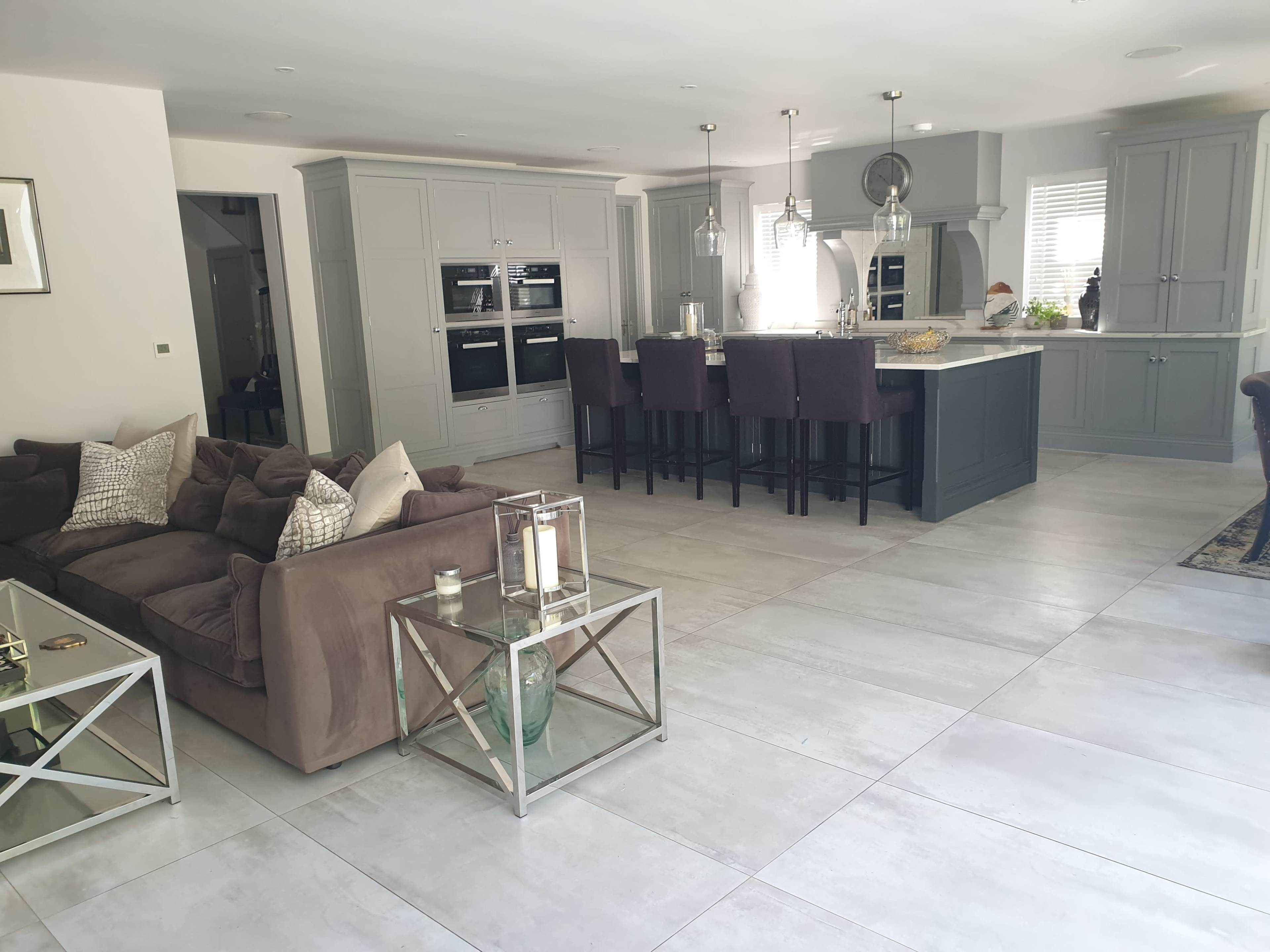 A modern, open-concept living space featuring a kitchen with dark cabinetry and bar stools, adjacent to a living area with a large sofa and glass coffee tables.