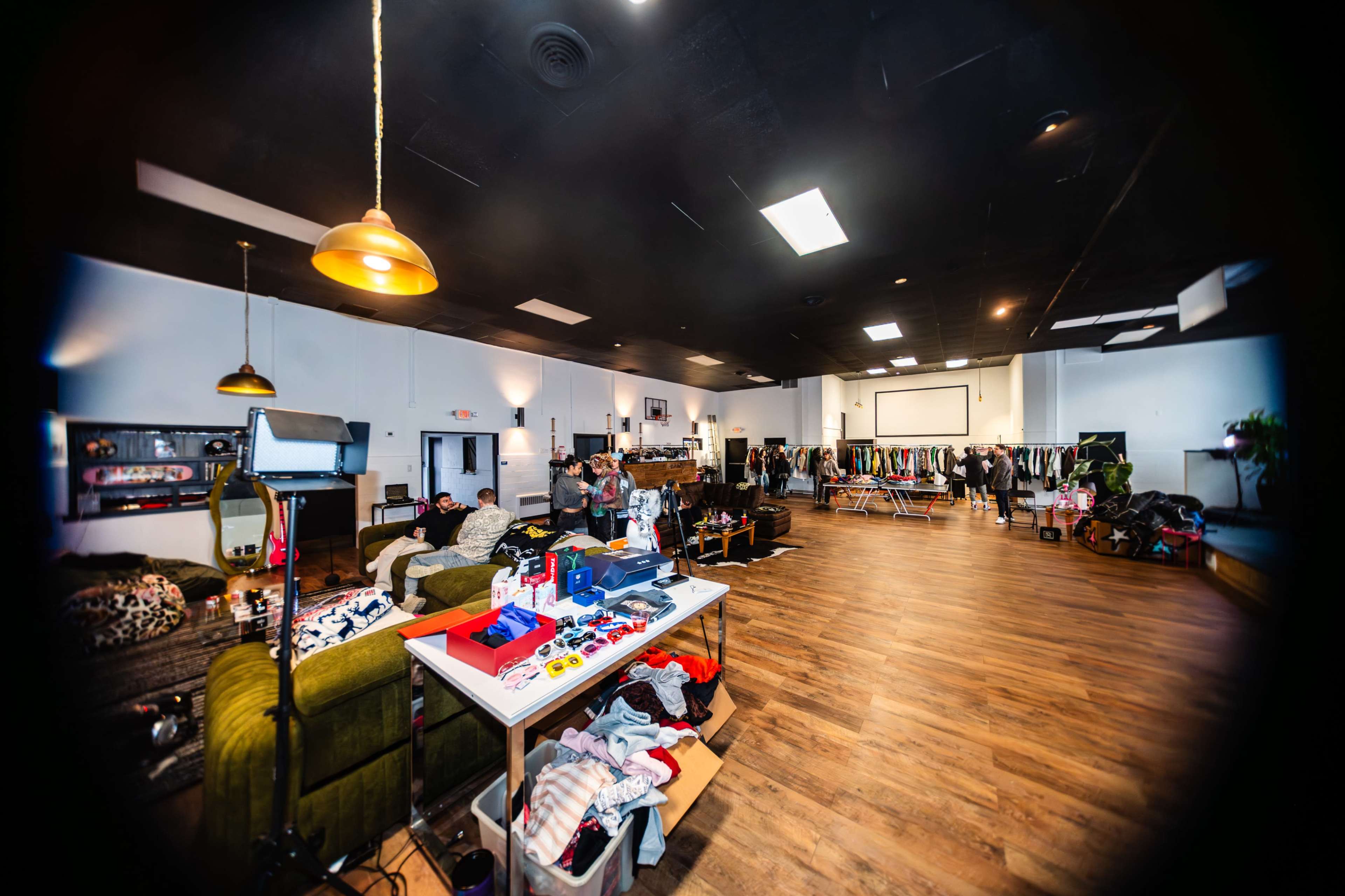 The image shows a spacious room featuring a clothing rack, various items on tables, and a group of people in the background.