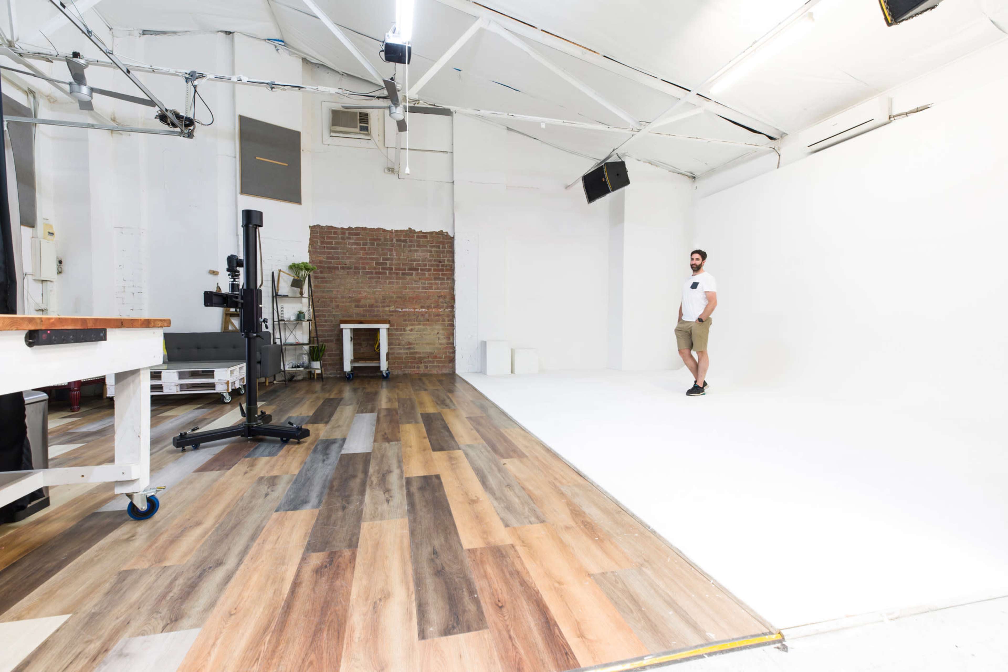 A man stands in a photography studio featuring a white backdrop and a hardwood floor with varying tones.