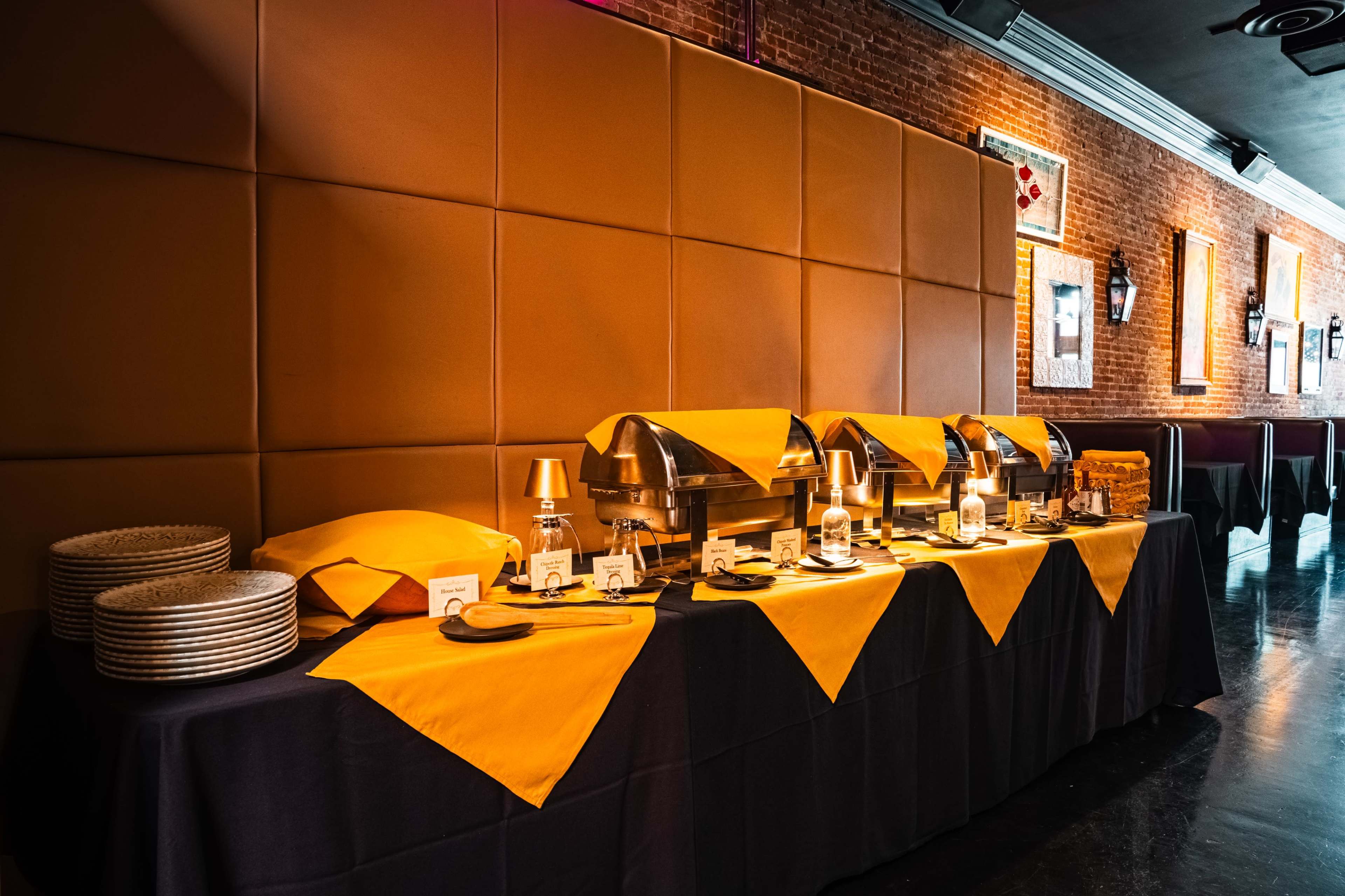 A buffet table adorned with yellow and black tablecloths features silver chafing dishes and neatly arranged plates.