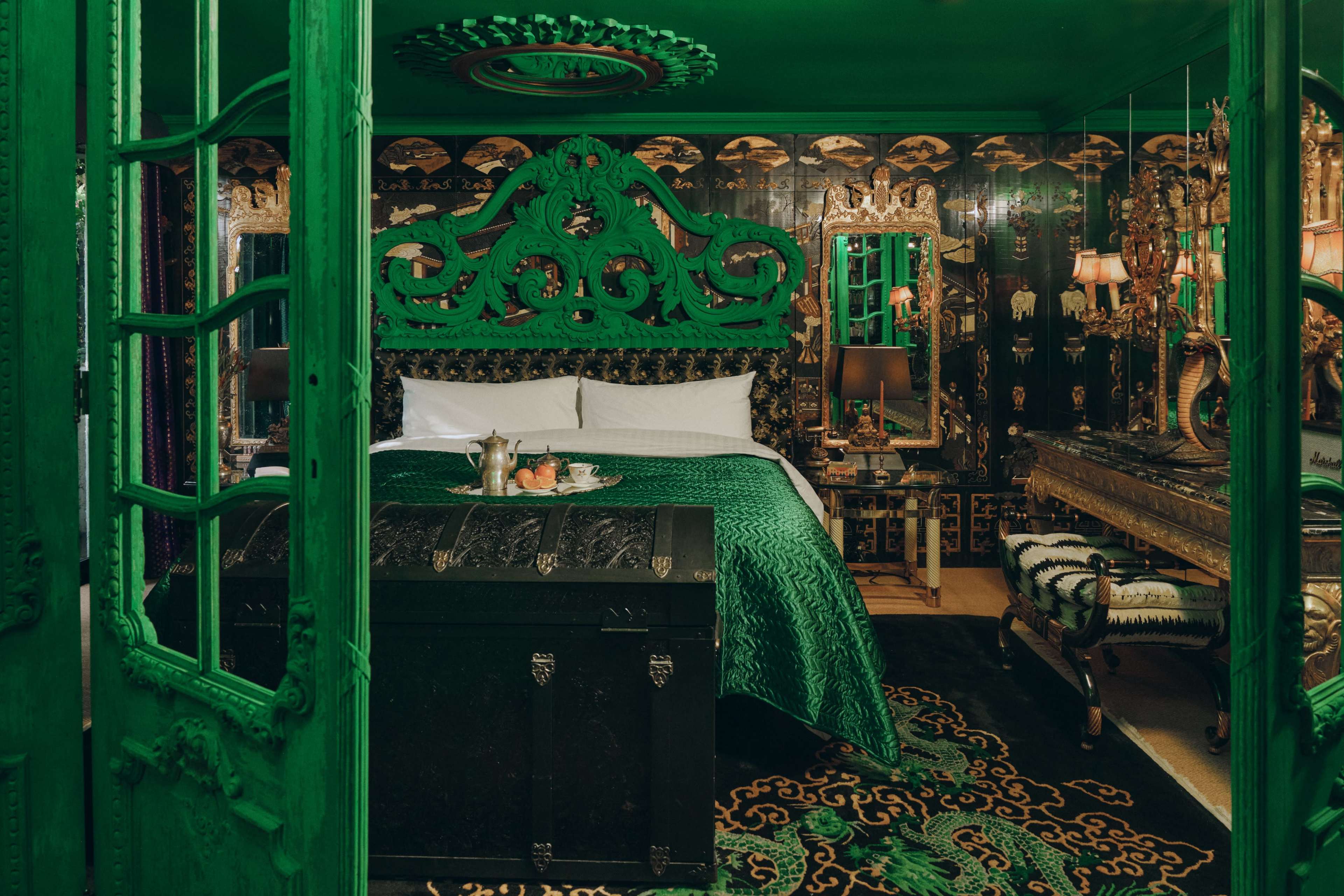 The image depicts a richly decorated bedroom featuring a green color scheme, ornate furnishings, and intricate wallpaper.