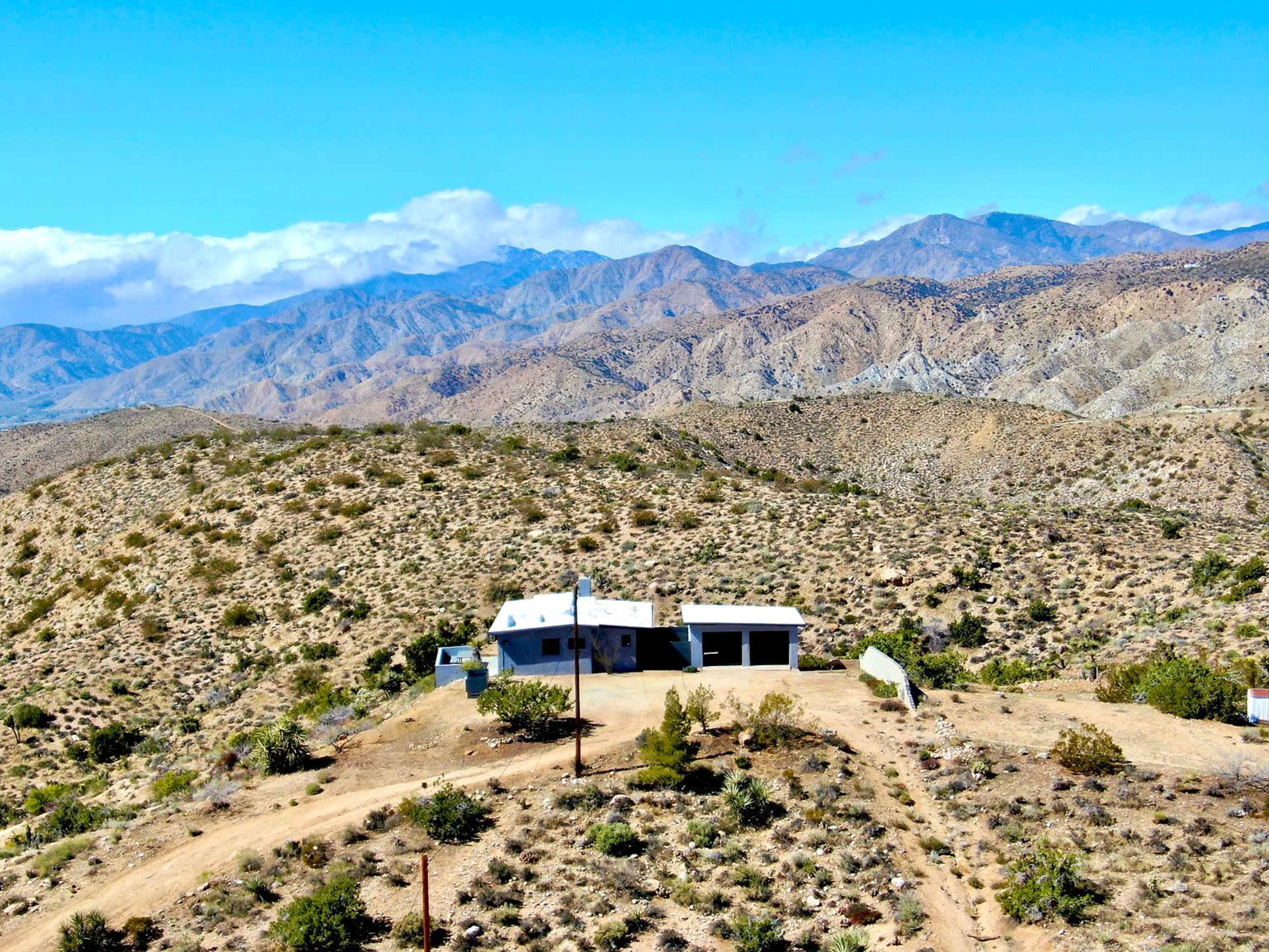 A small building is situated in a mountainous desert landscape, surrounded by sparse vegetation and rocky terrain.