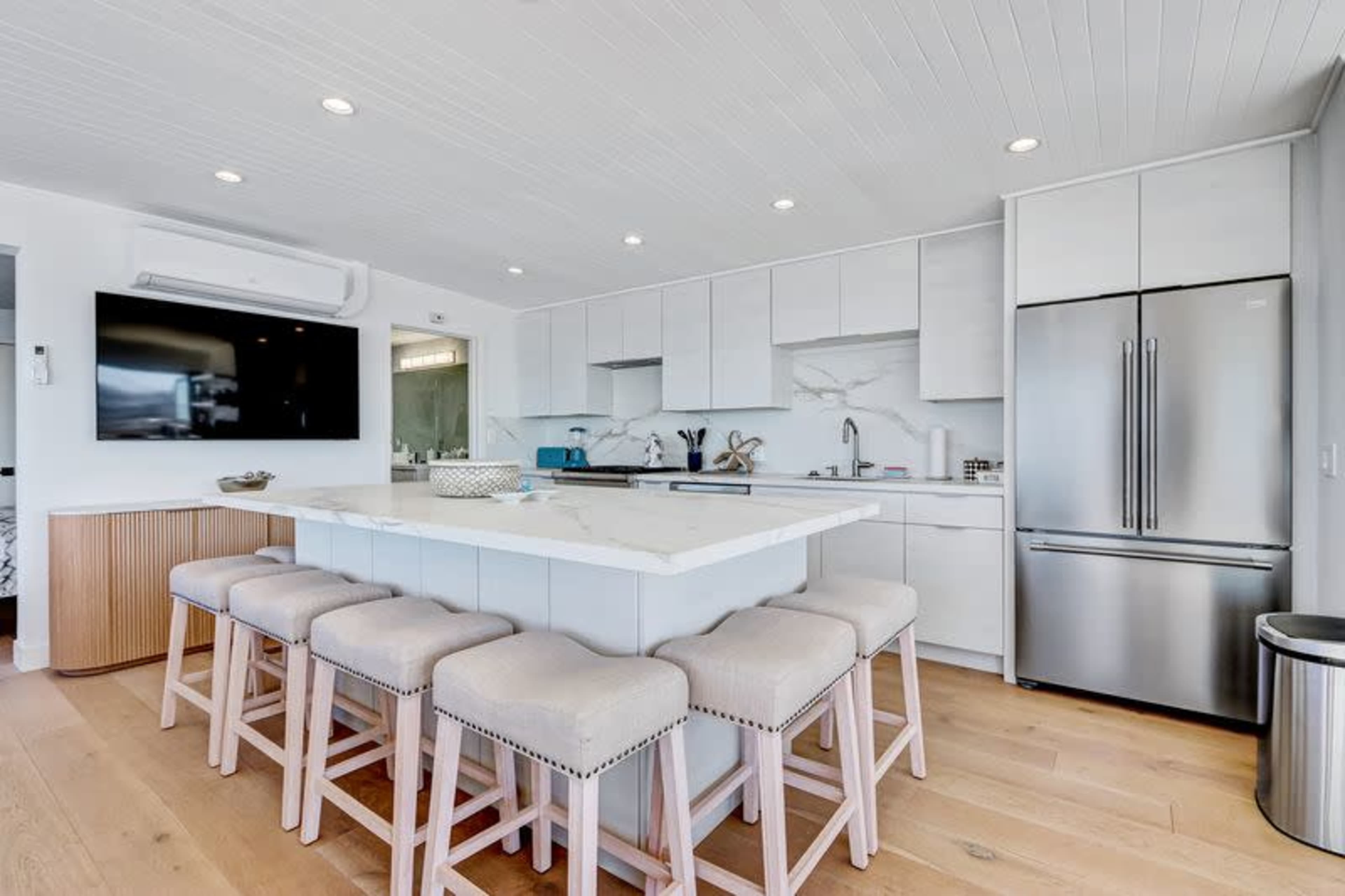 The image shows a modern kitchen with a large island, stainless steel appliances, and light wood flooring.