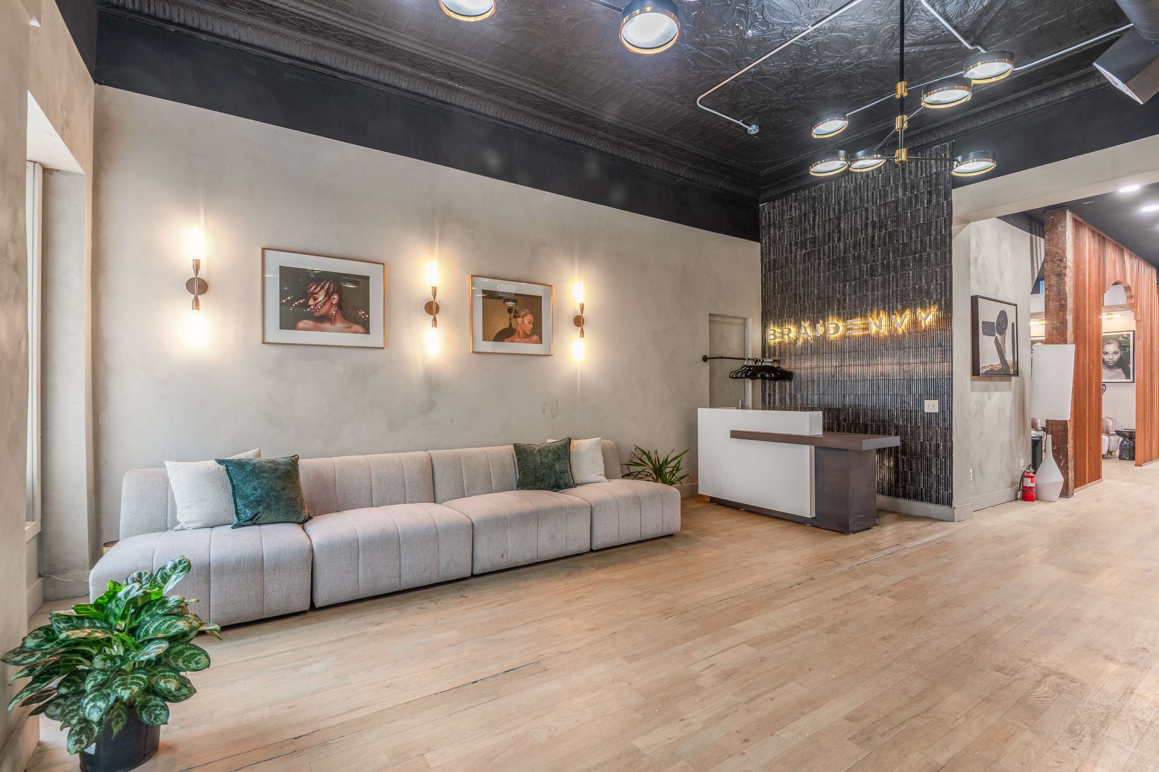 The image shows a modern interior space featuring a light-colored sofa, framed artwork on the walls, and a reception area with a wooden counter.