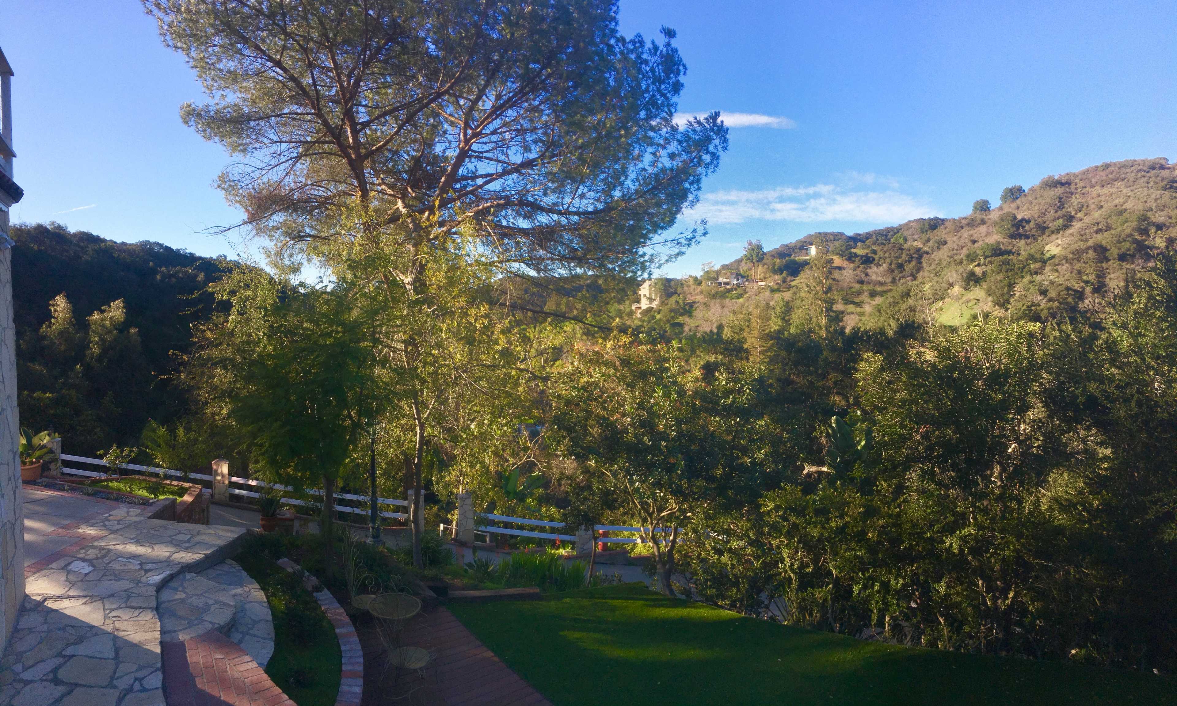 A landscaped garden with stone paths, lush greenery, and distant hills under a blue sky.